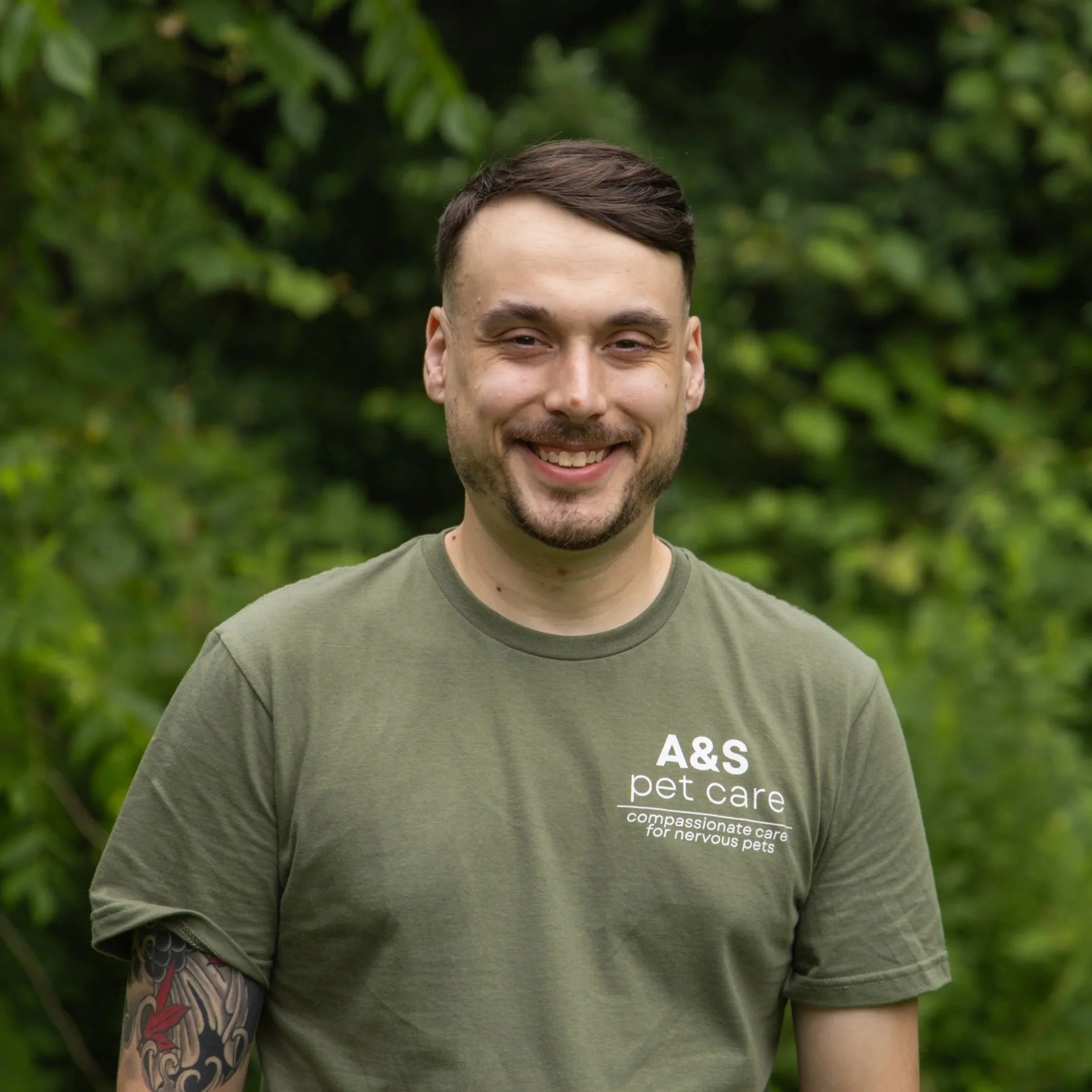 A man holding a happy, smiling dog with its tongue out in a forest setting.