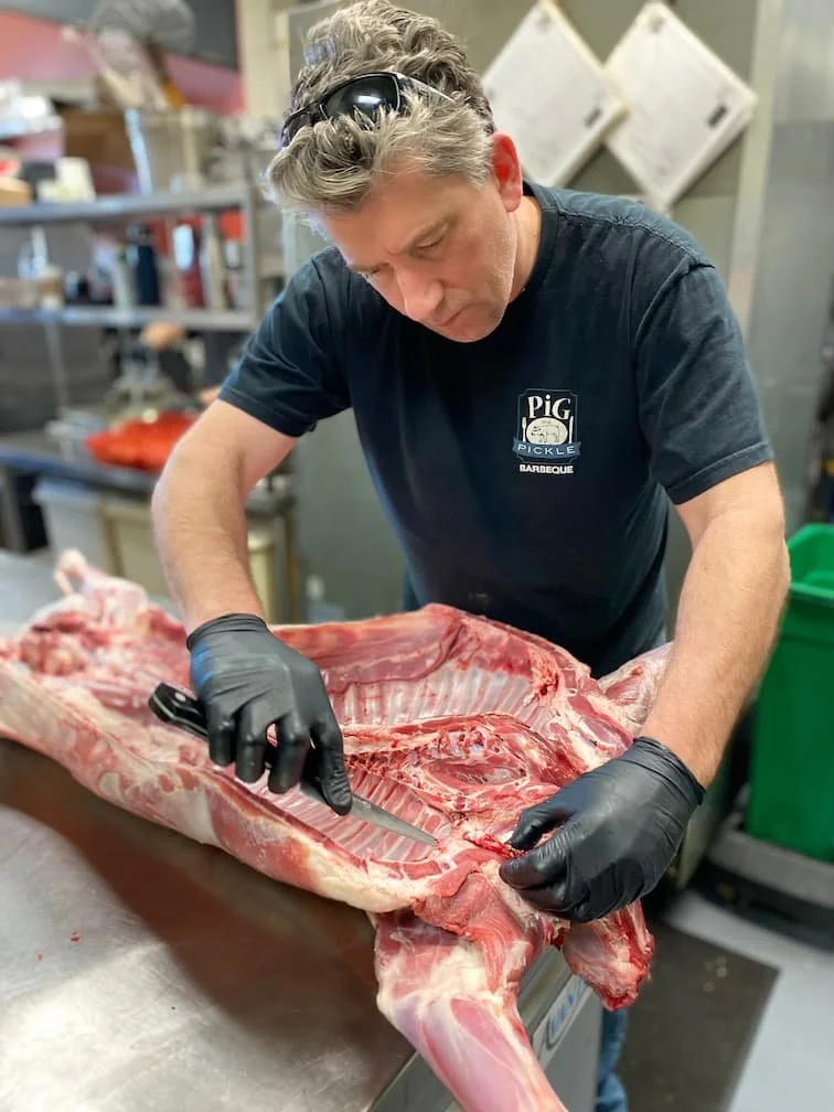 Chef Damon demonstrates his expert butchery skills, carefully preparing premium cuts of sustainably-sourced meat in the kitchen at Pig & Pickle Barbecue