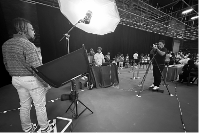 Photographers setting up equipment in a dark studio for a photoshoot or filming session.