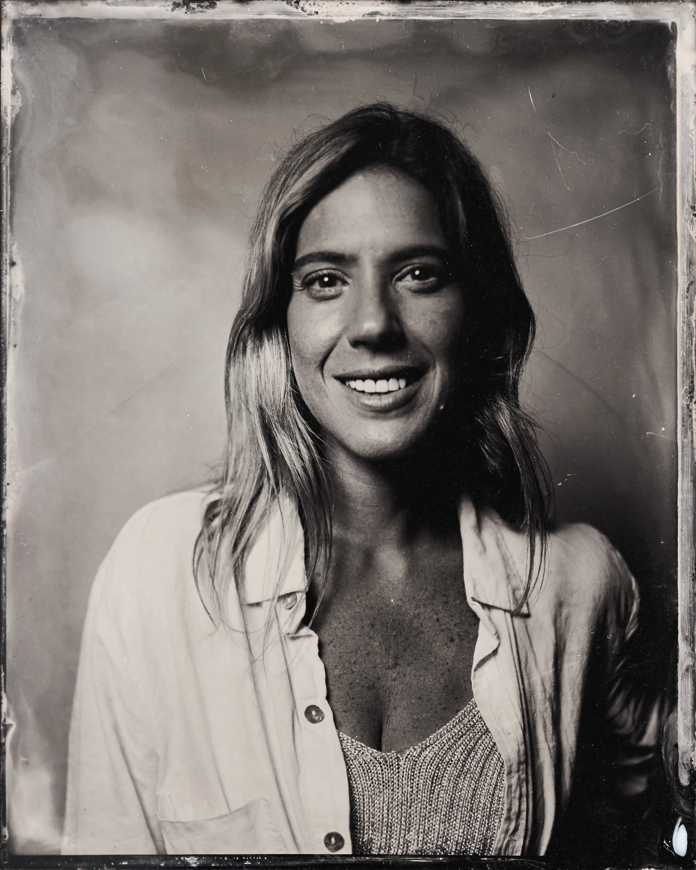 Black and white photo of a smiling woman with wavy hair, wearing a button-up shirt over a textured top, against a plain background.