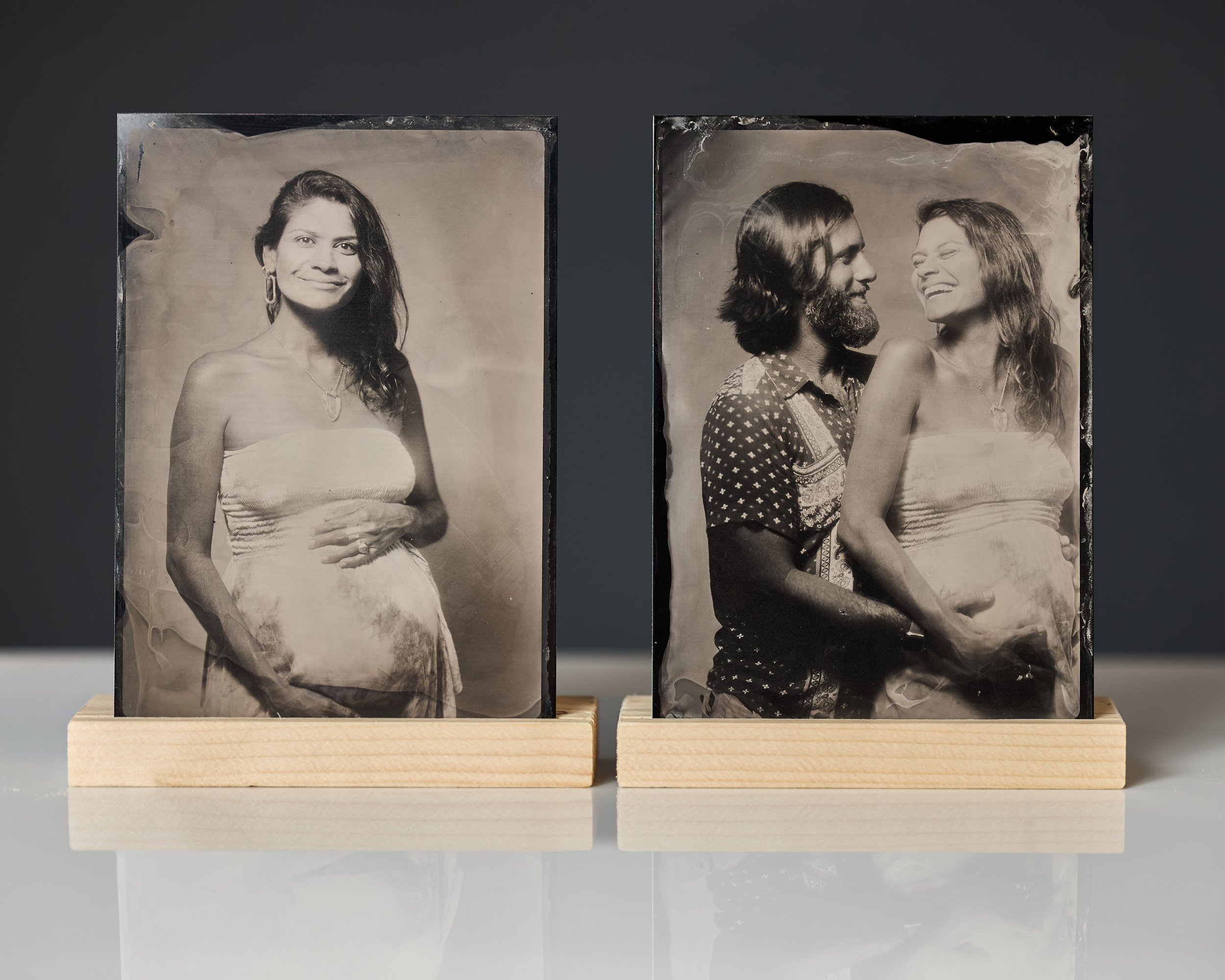Two vintage black-and-white photographs of a pregnant woman, one solo and one with a partner, displayed on wooden stands against a dark background.