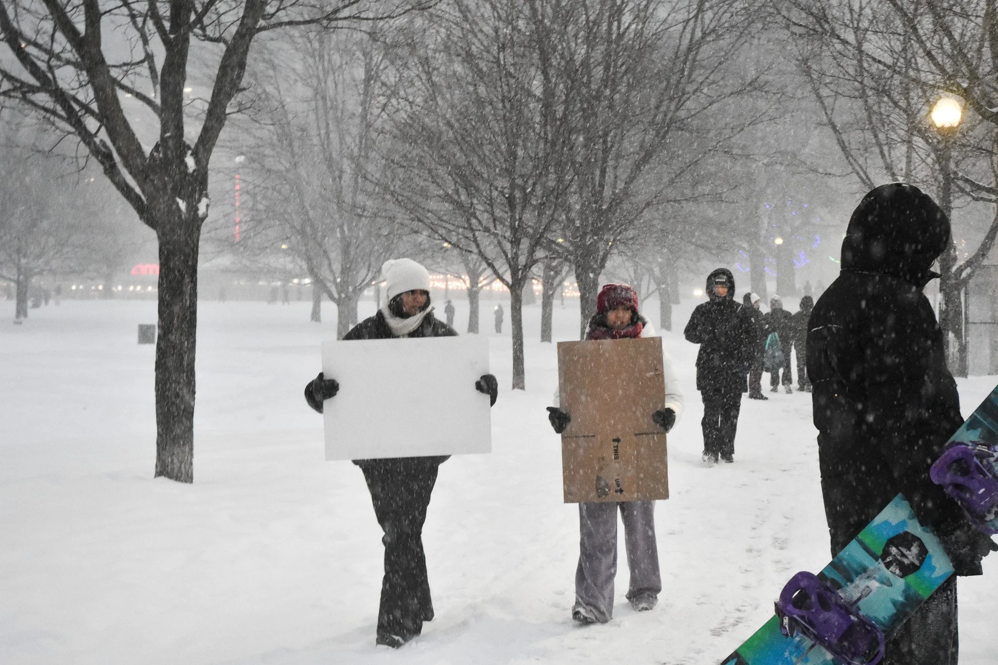 Boston, MA: Jan. 25 -  Two people with flattened cardboard boxes walk towards the hill, hoping their makeshift sleds work. 