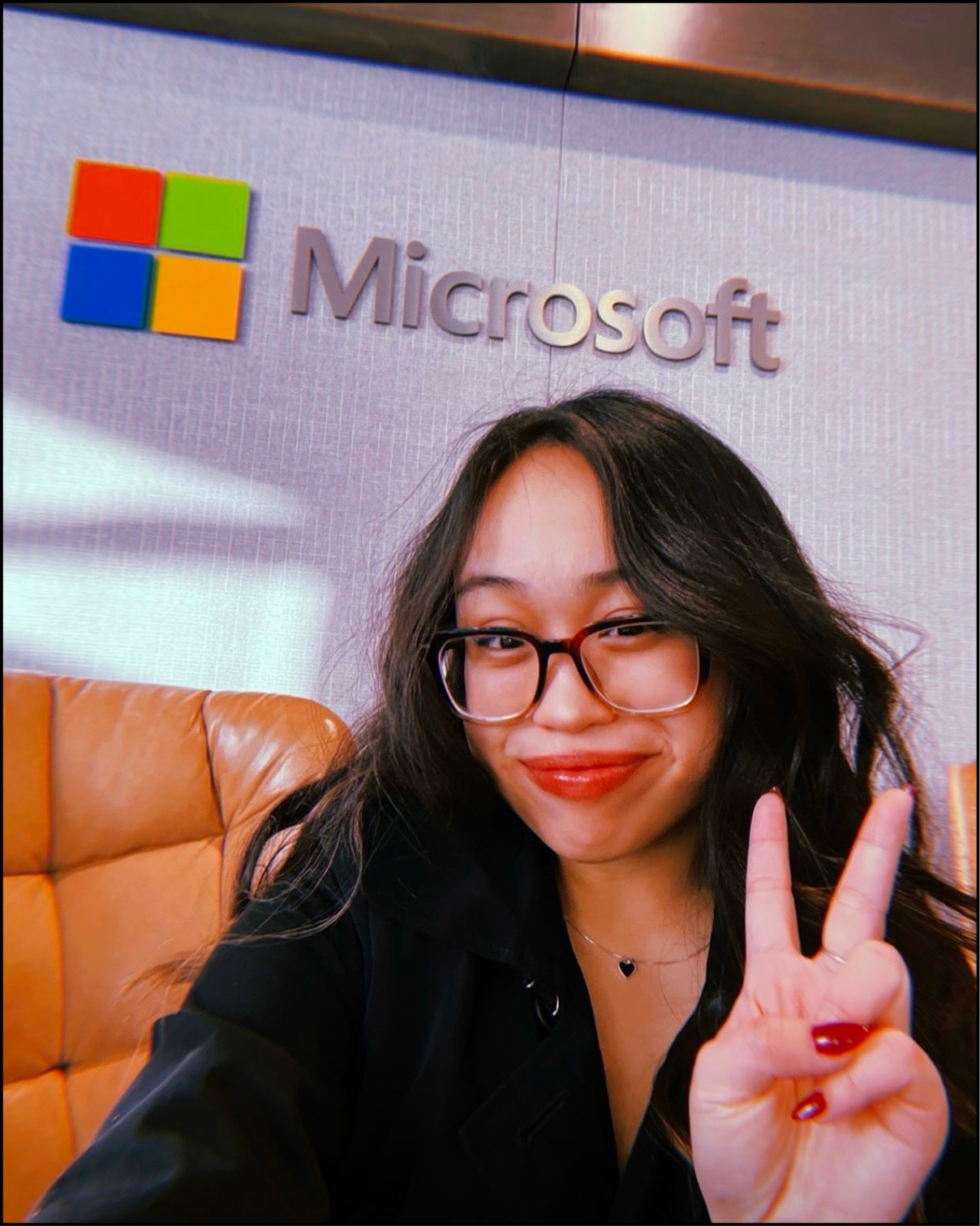 Woman with glasses making a peace sign in front of a Microsoft sign.