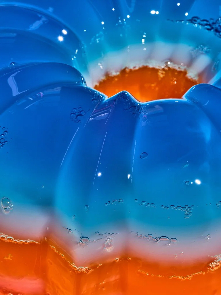 Close-up of a layered Gatorade jelly Bundt, with translucent electric-blue jelly above a bright orange layer and small bubbles suspended throughout