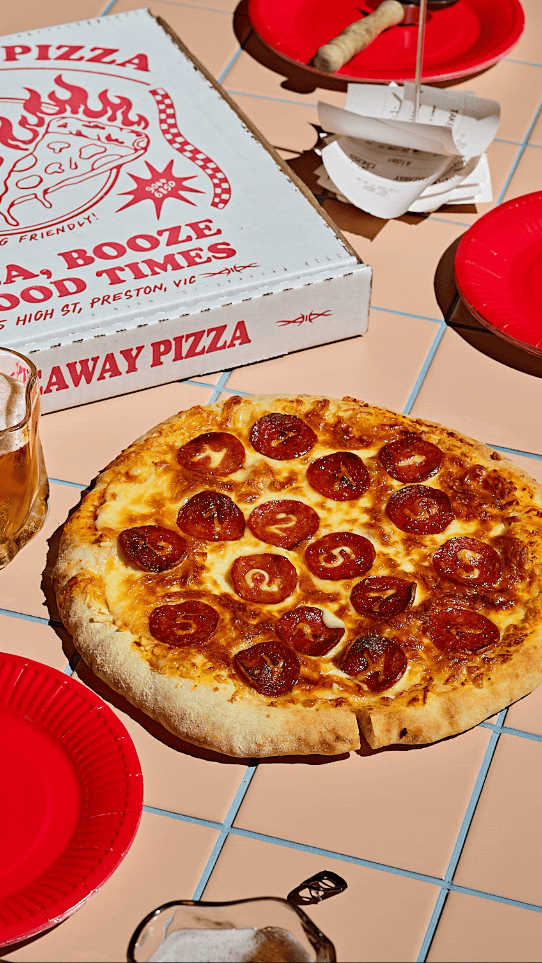 Whole pepperoni pizza on a tiled table beside a takeaway pizza box, red paper plates and a restaurant bill, photographed to announce $125,000 in charitable donations through the Pierogi Studio Fund.