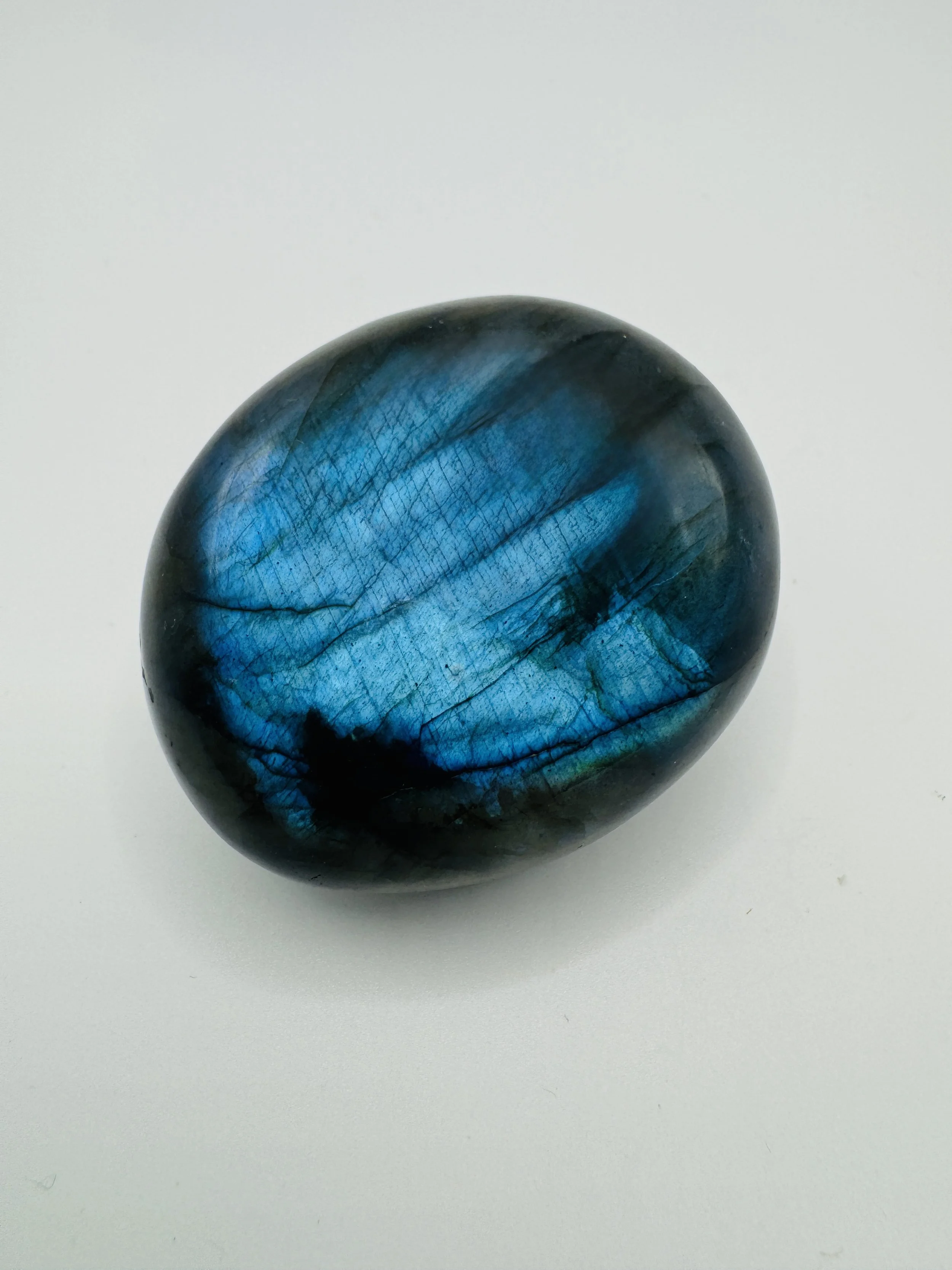 A polished labradorite sphere showing vibrant blue and green iridescence on a white background.
