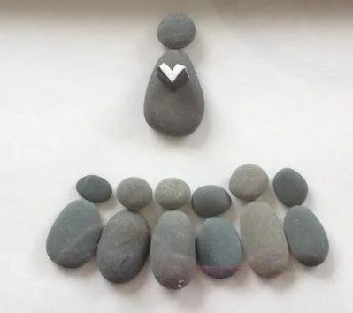 Arrangement of smooth, rounded stones on a flat surface, with some stacked to resemble a figure.