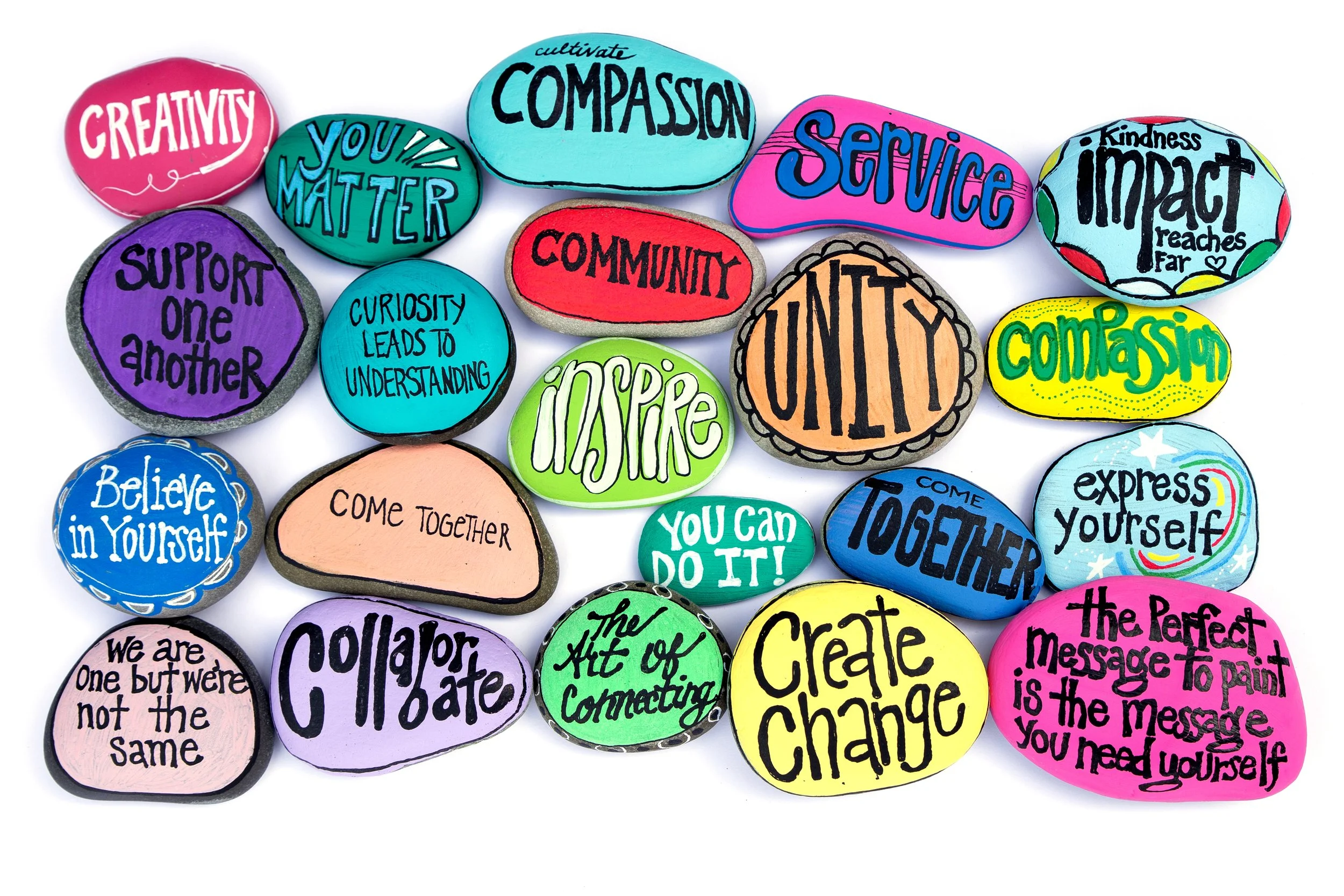 Colorful painted rocks with inspiring words and phrases related to kindness, community, and self-improvement, such as 'Creativity,' 'Compassion,' 'Support one another,' and 'Create change.'