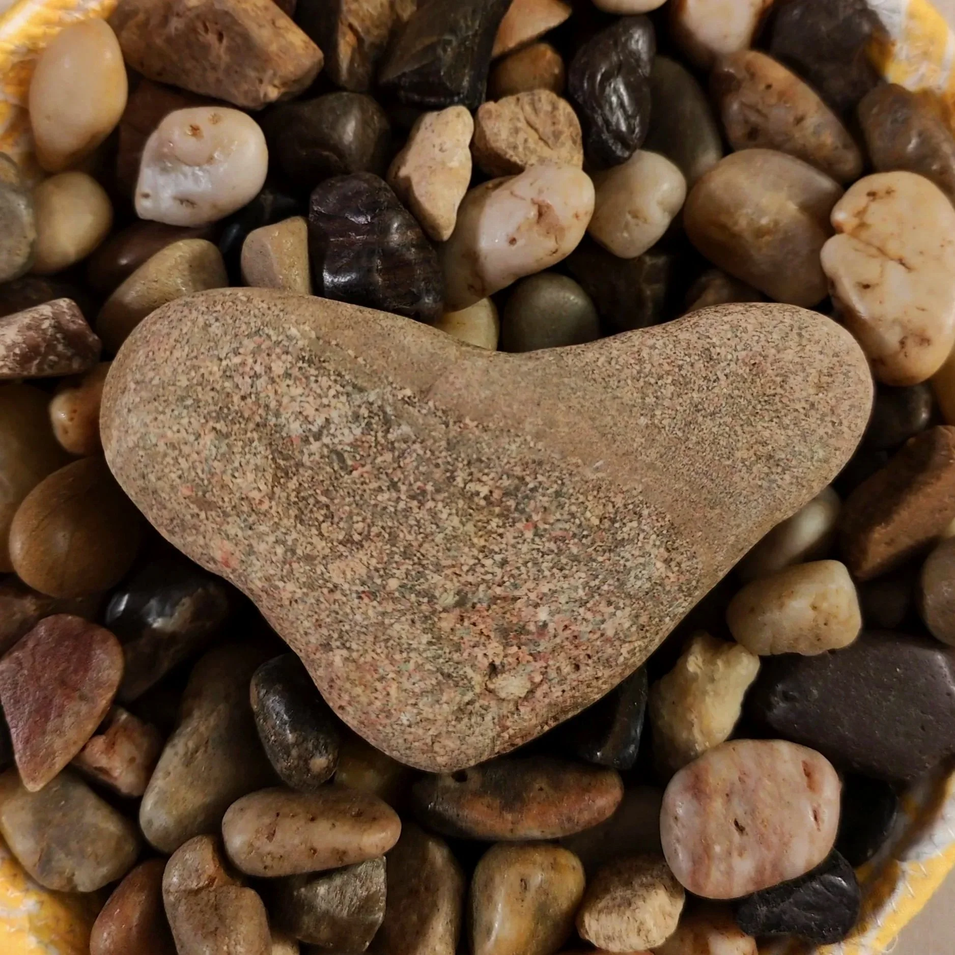 A large, smooth, heart-shaped stone resting on smaller multicolored pebbles.
