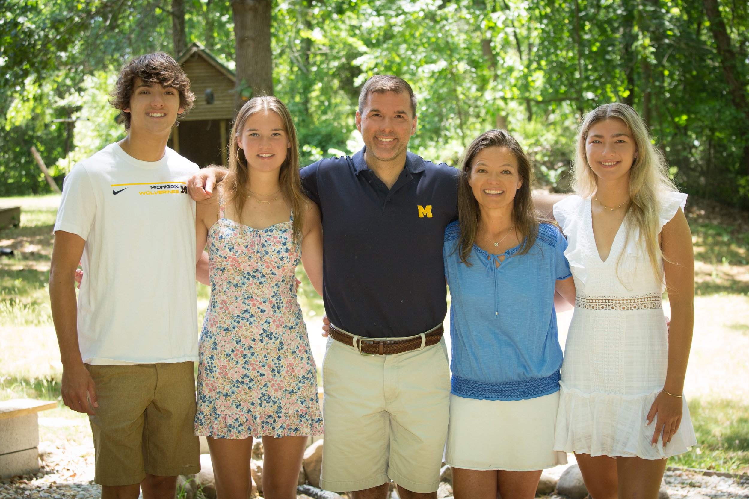 Group of five people standing outdoors with trees in the background, smiling and posing for a photo.