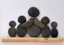 Stacked black and gray stones arranged to resemble a face with a mustache, on a wooden surface.