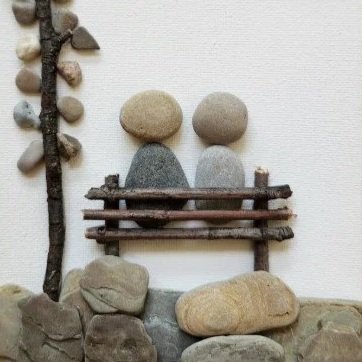 Art installation resembling a face made of rocks, sticks, and a wall with some rocks on the ground.