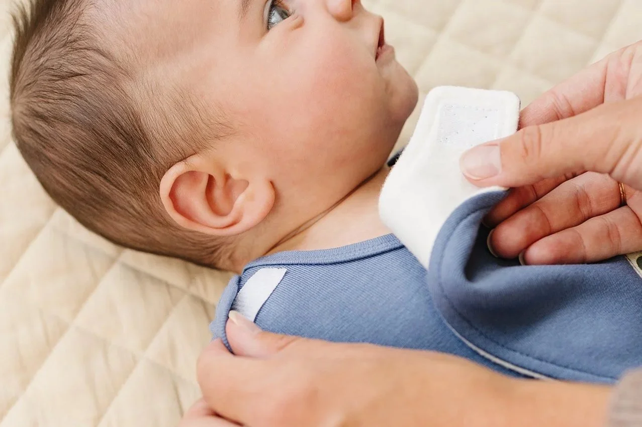 Caregiver fastening a quick-change bib on a baby lying on a quilted mat.