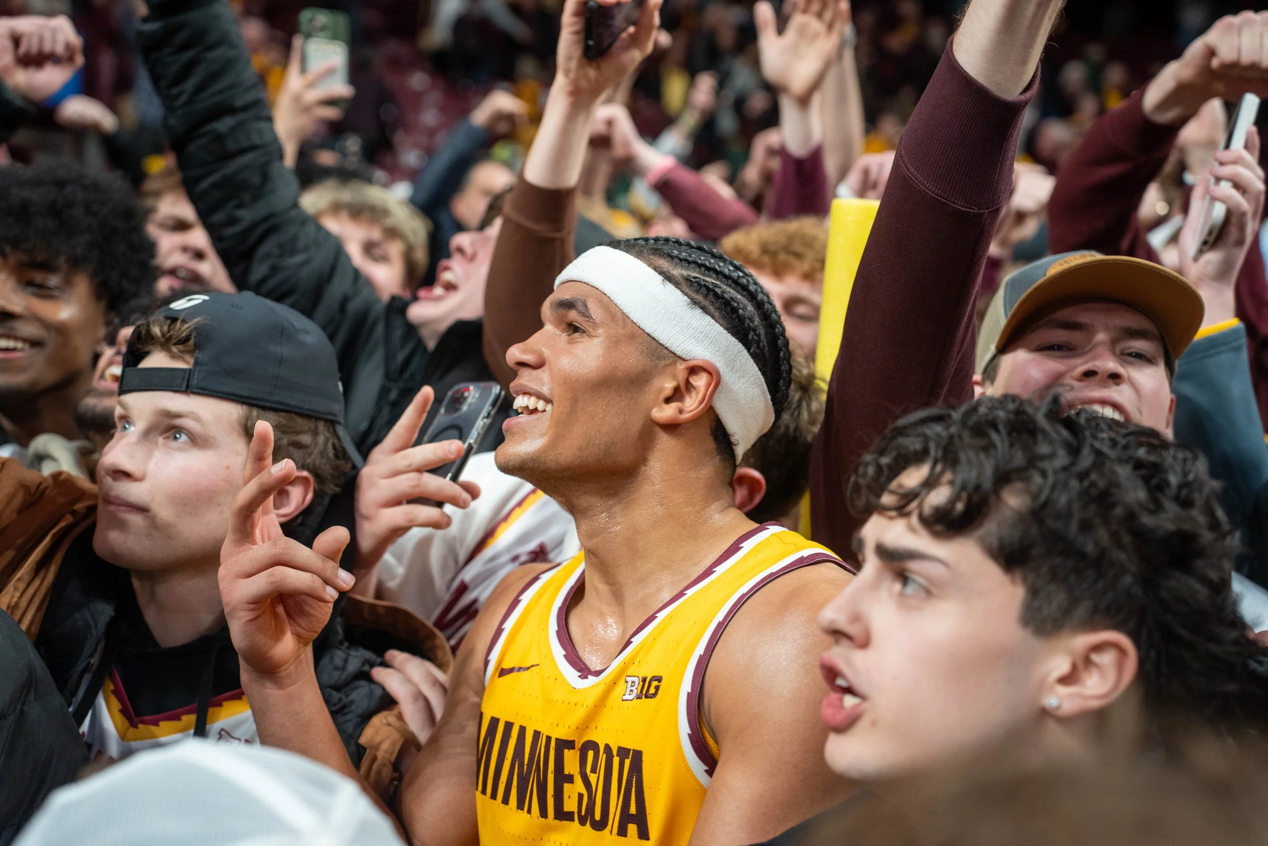 Crowd of excited fans at a sports event, with a basketball player wearing a yellow and maroon jersey labeled 'Minnesota' in the foreground.