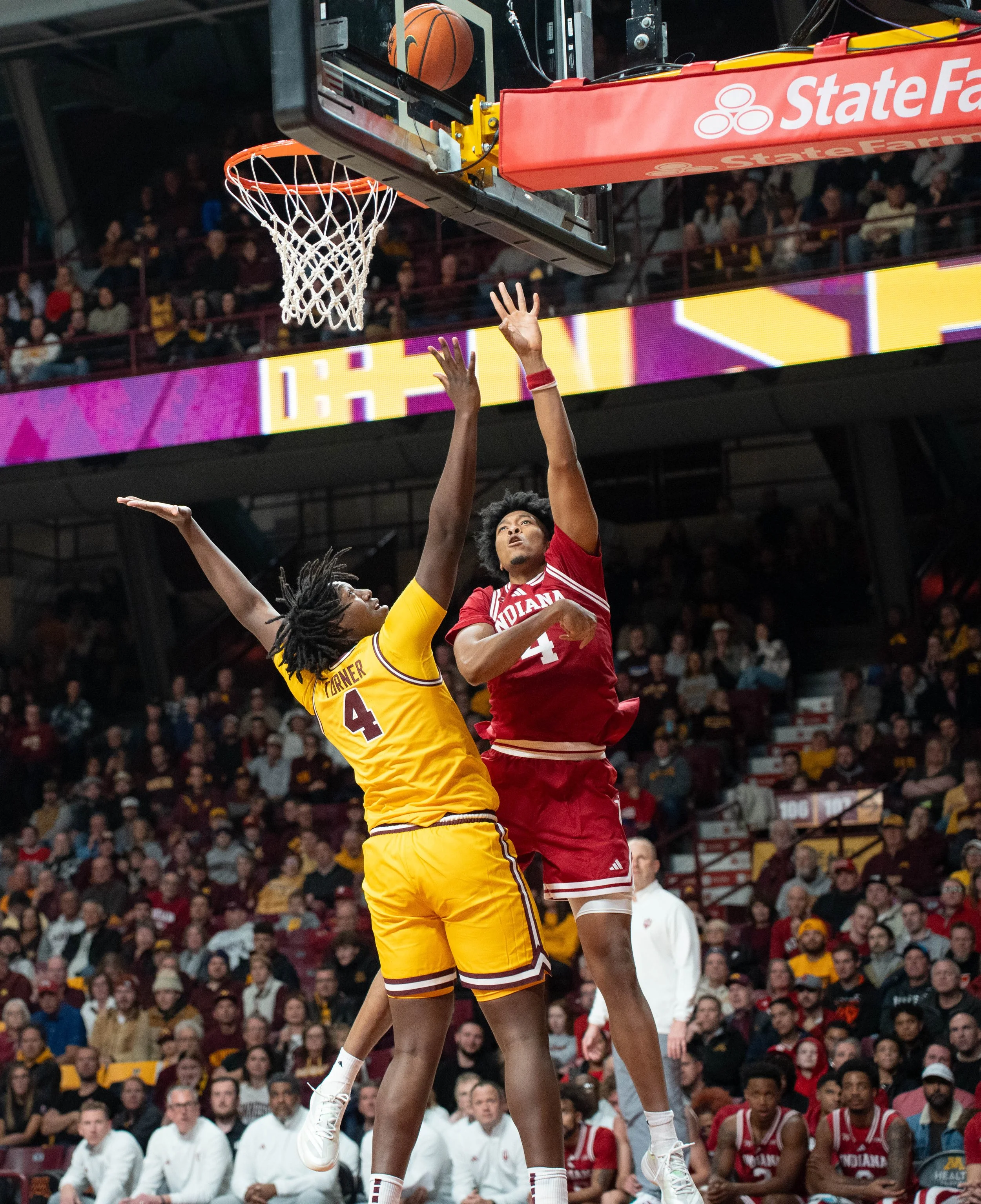 Two basketball players jumping near the hoop during a game with a crowd in the background.