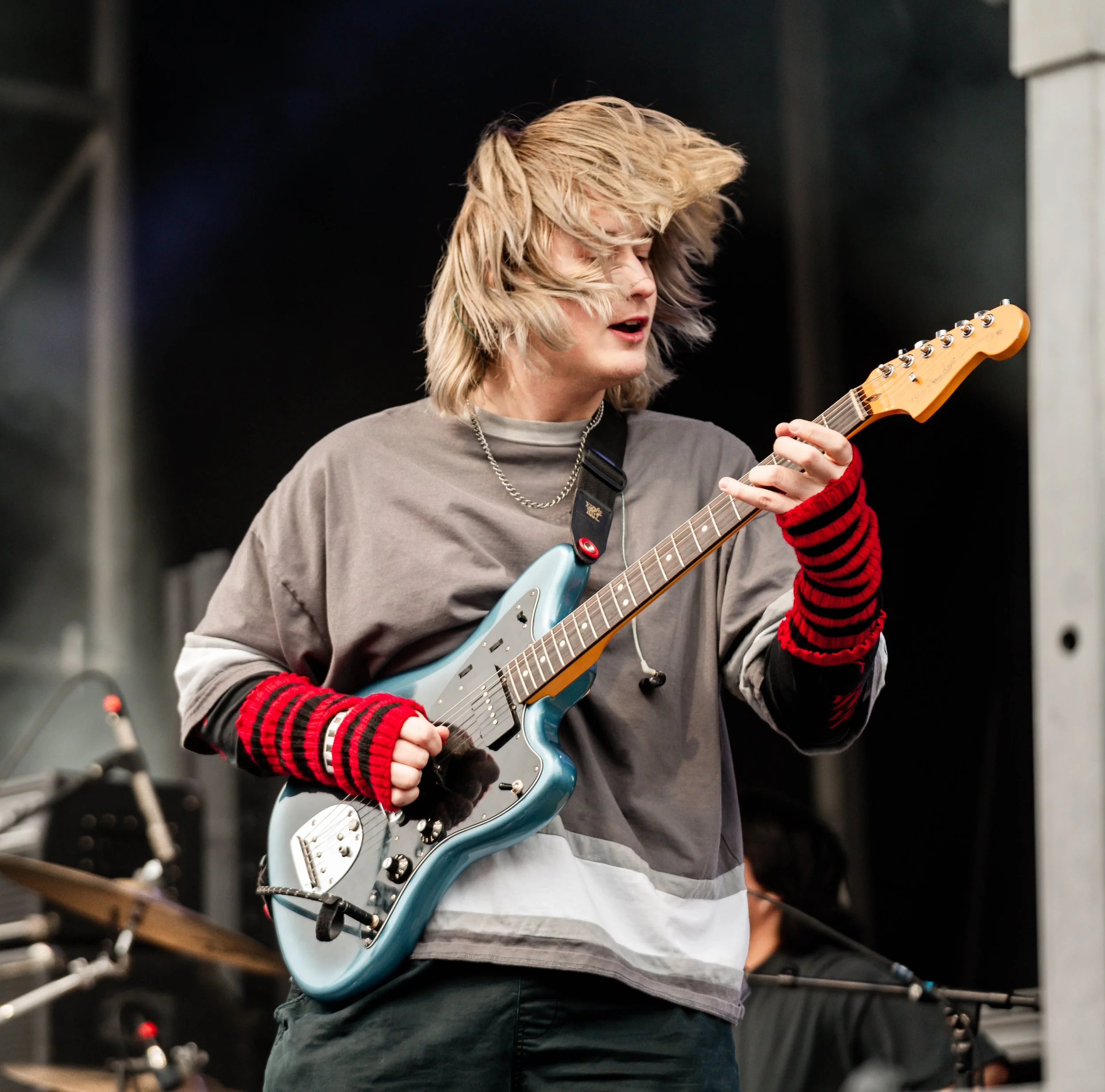 Person with blonde hair playing an electric guitar in a music studio or rehearsal space.