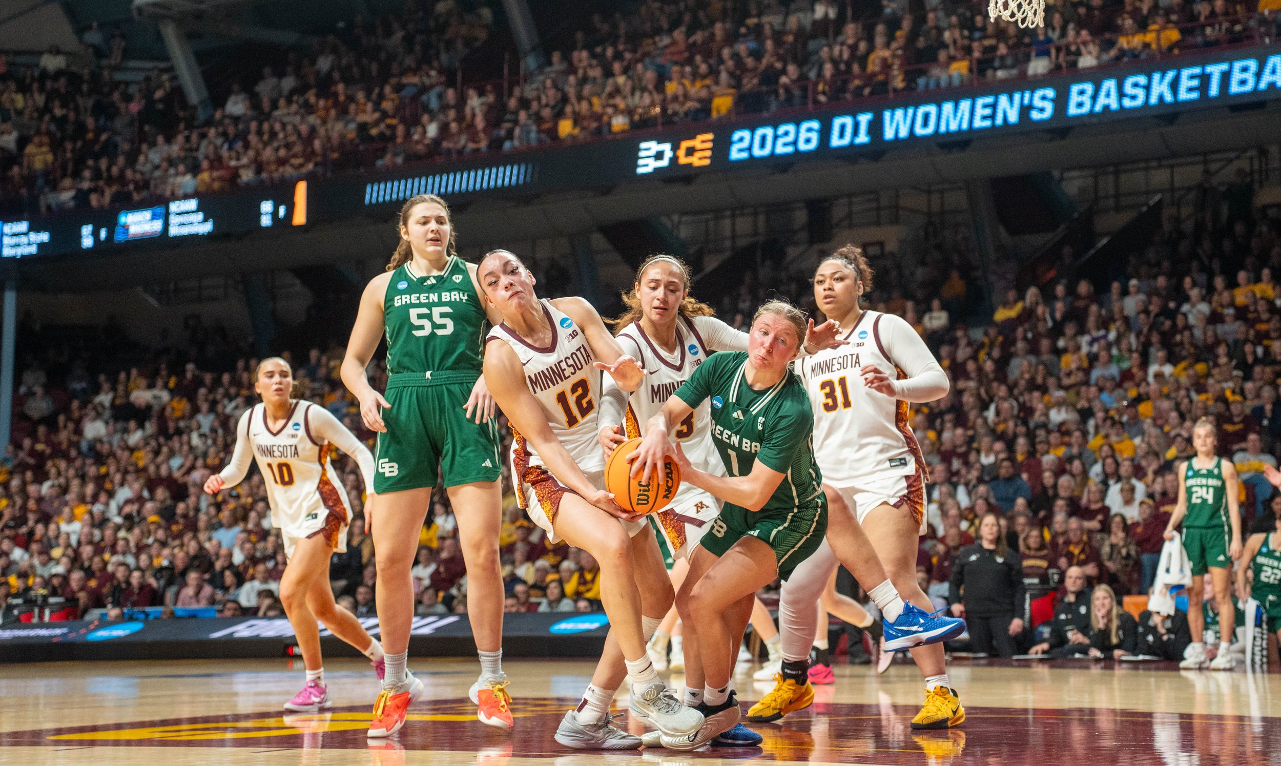 Women’s basketball game with players from Green Bay and Minnesota battling for possession of the ball on court filled with spectators.