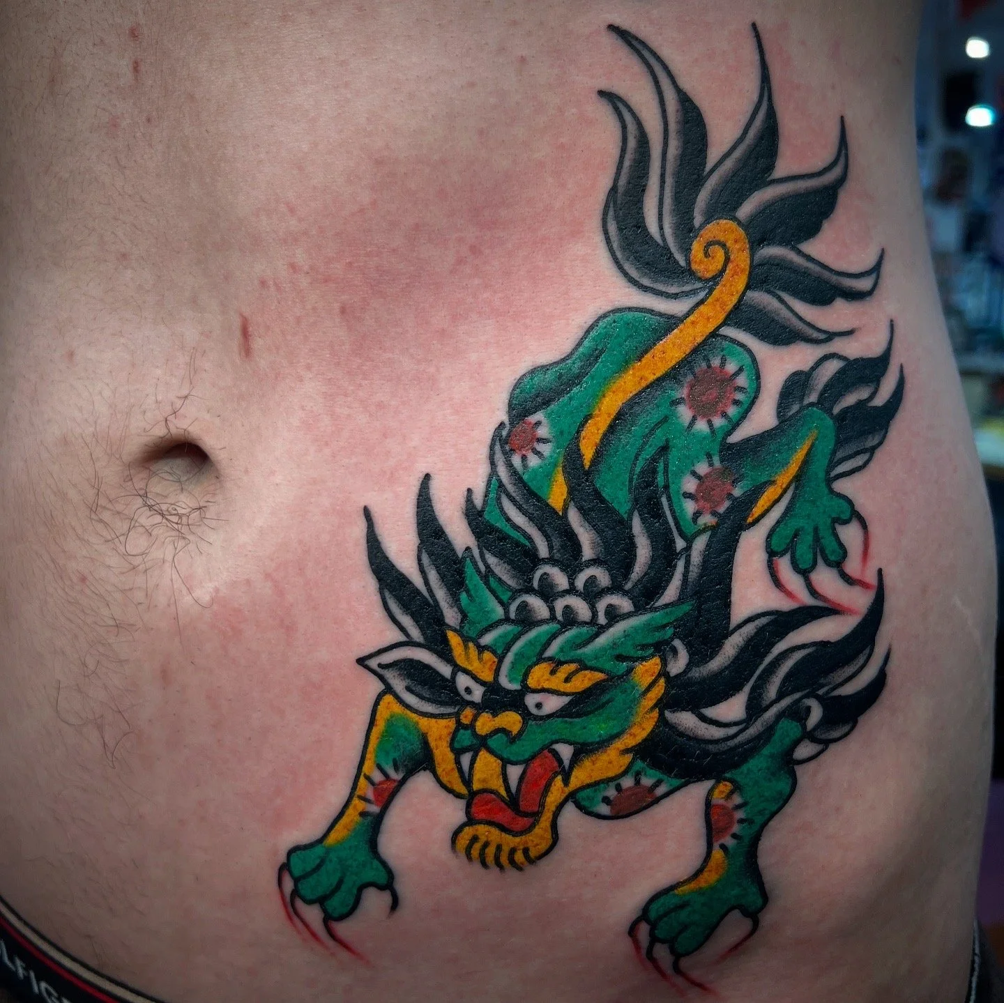 Tattoo of a fierce, multicolored dragon with green, black, yellow, and red details on a person's chest near the armpit.
