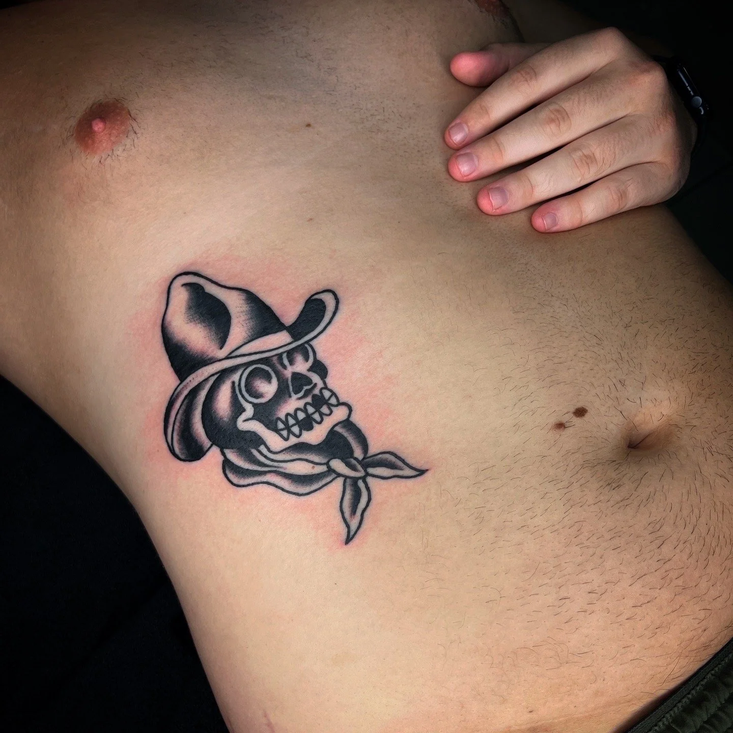 Tattoo of a skull wearing a cowboy hat and bandana, located on the person's upper chest or shoulder area.