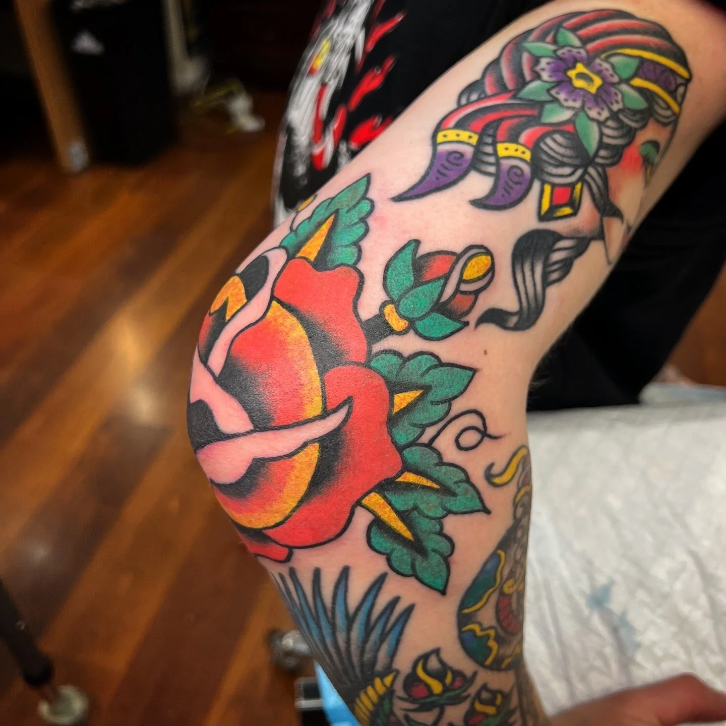 Colorful tattoo of a rose with green leaves on a person's arm.