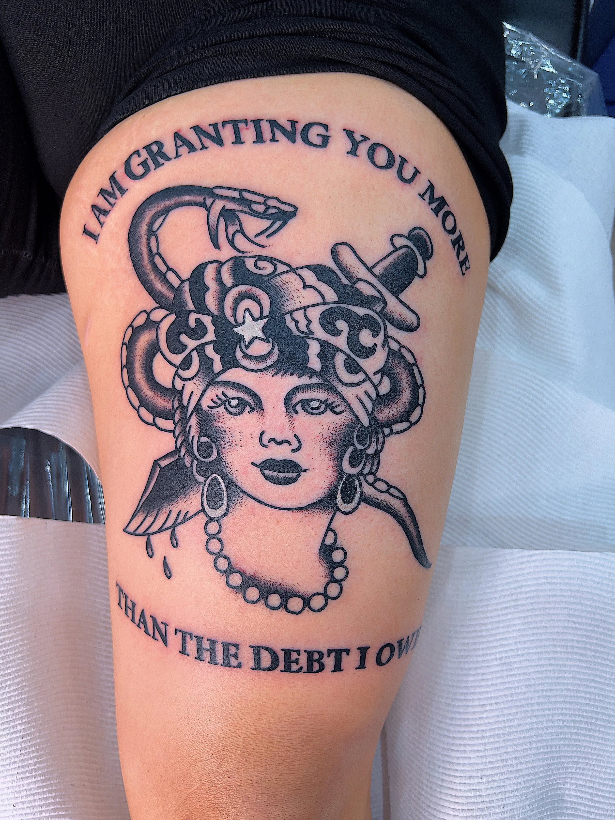 Tattoo of a woman's face with snake hair, a dagger, and the text 'I am granting you more than the debt I owe'