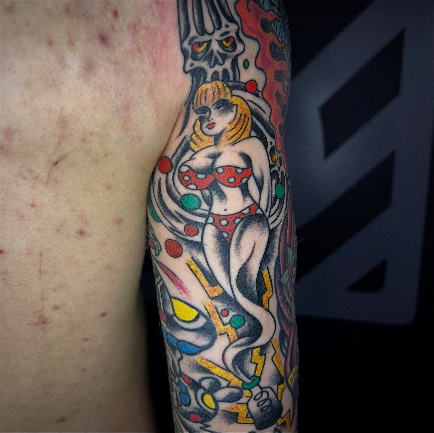 Tattoo sleeve featuring a vintage pin-up style woman in a red polka dot bikini and a snake coiled around her. The tattoo includes bold colors, black outlines, and some lightning bolt elements.