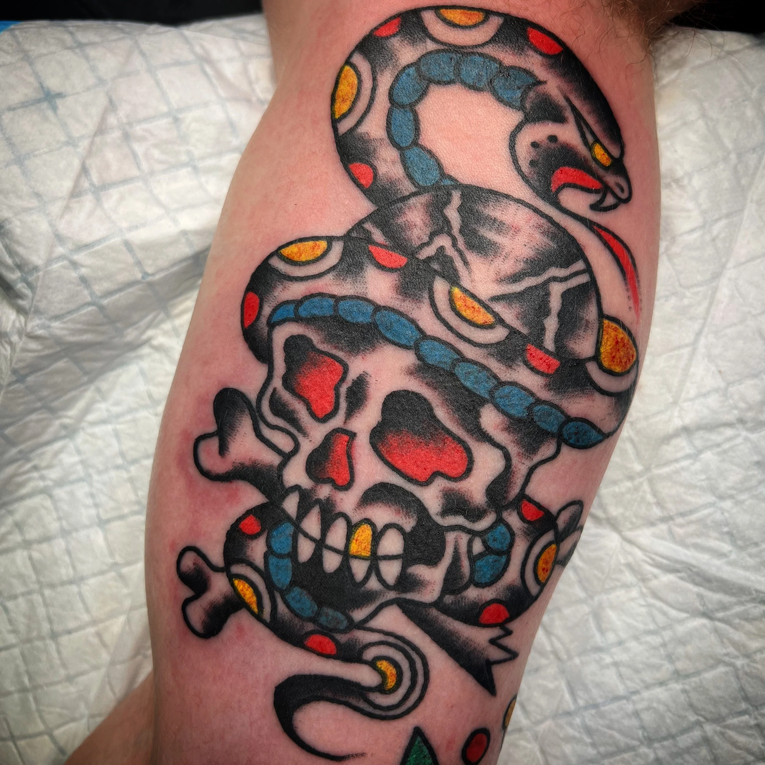 Tattoo of a skull with a snake wrapped around it, featuring red, yellow, blue, and black colors.