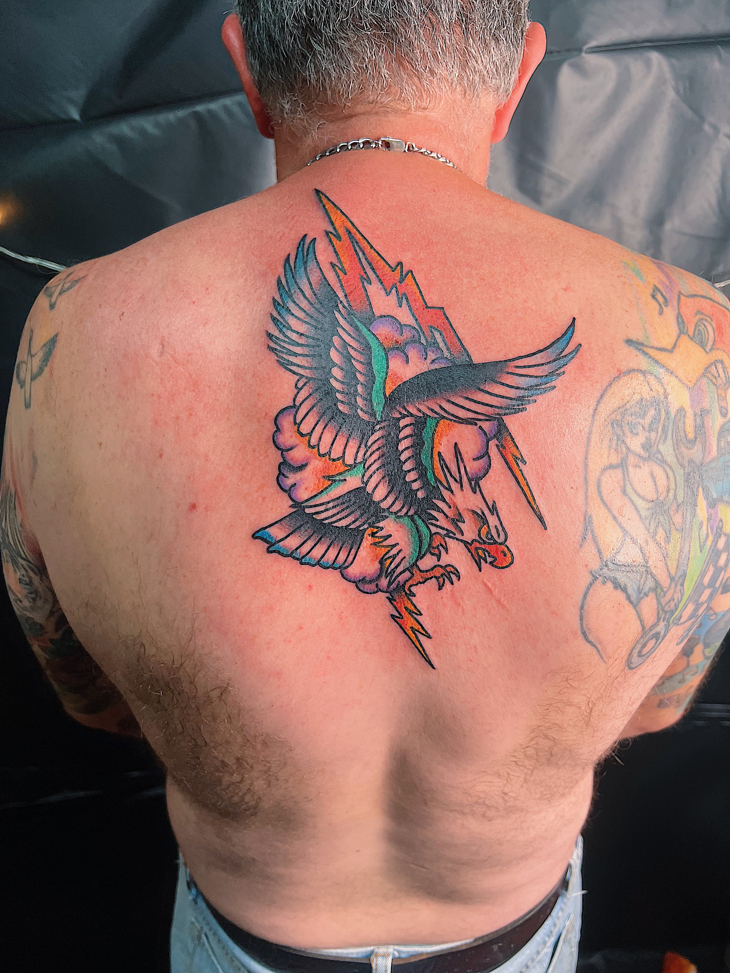 Tattoo of a dragon with lightning bolts and clouds on a person's upper back.