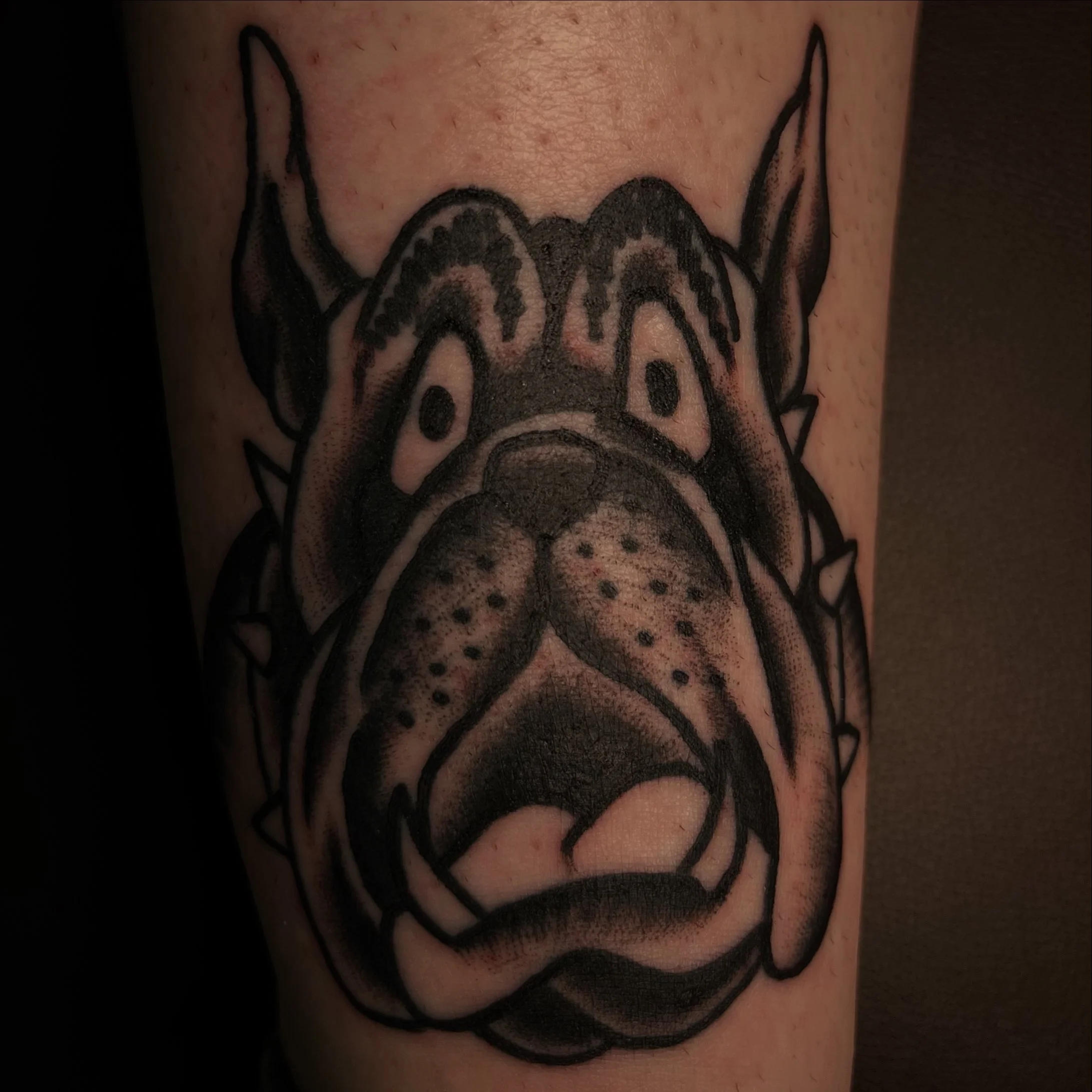 Black and gray tattoo of a dog's face with expressive eyes and tongue out on person's arm.