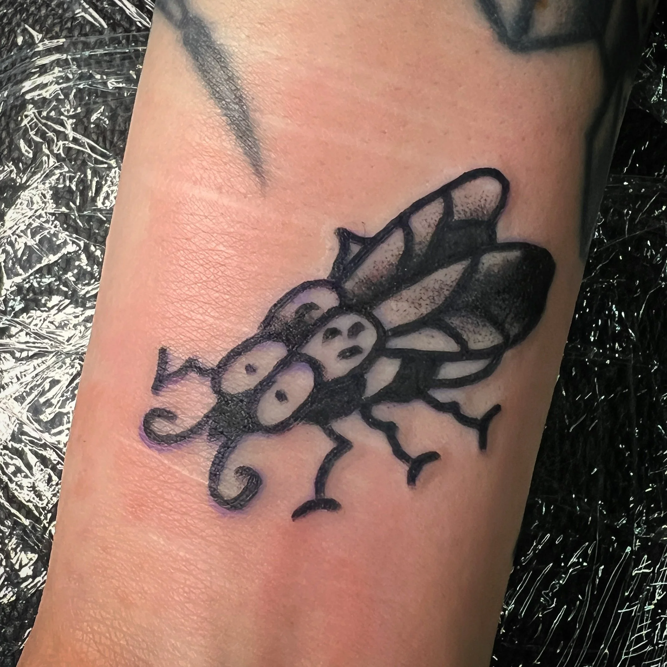 Tattoo of a bee with stylized wings on a person's forearm.