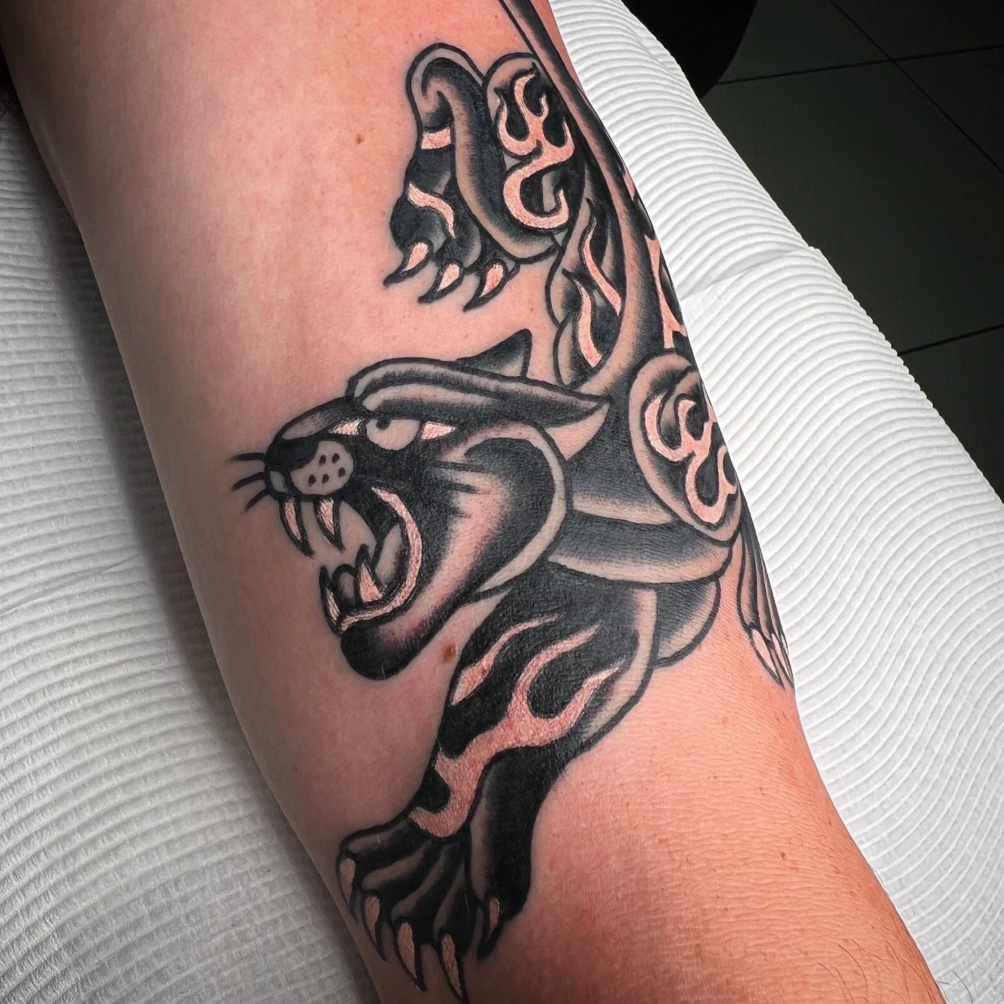 A black and gray tattoo of a fierce, roaring tiger's head with detailed shading and stylized flames or patterns on its body.