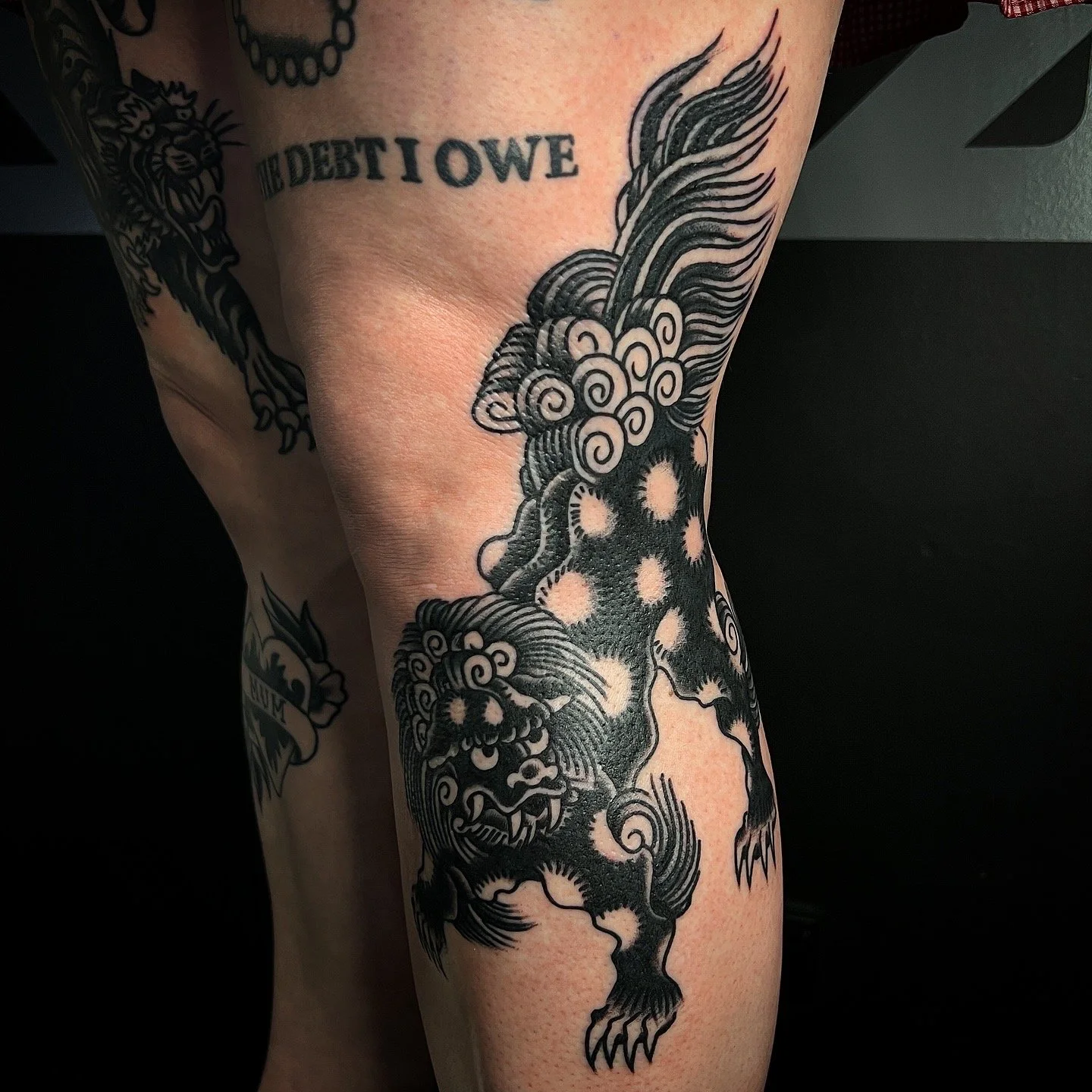 Tattoo of a fierce, stylized lion with flowing hair on a person's thigh, in black ink.