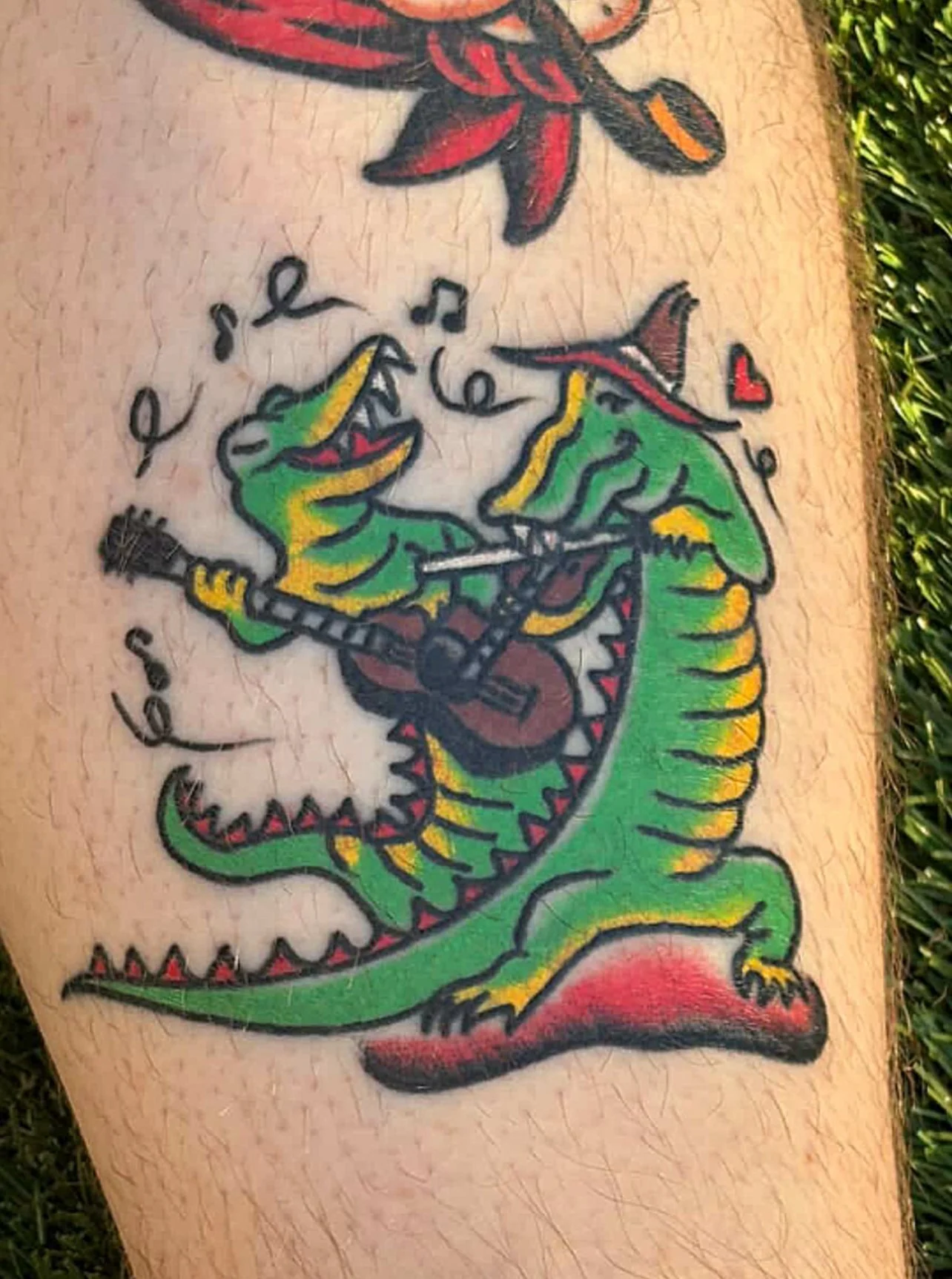 A colorful tattoo of a cartoon crocodile playing a guitar and singing with musical notes and hearts around it, on someone's arm.