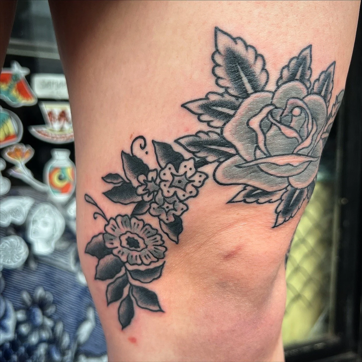 Black and gray flower tattoo on skin, featuring a rose, surrounded by smaller flowers and leaves.