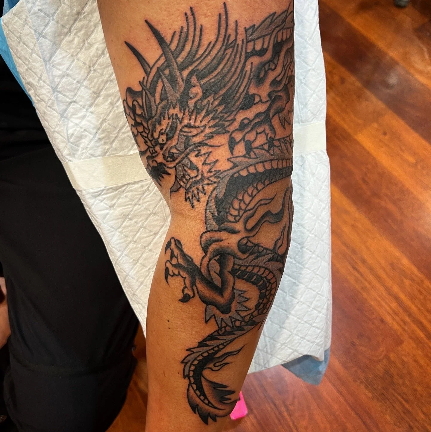 Black and gray tattoo of a fierce, detailed dragon on a person's arm.