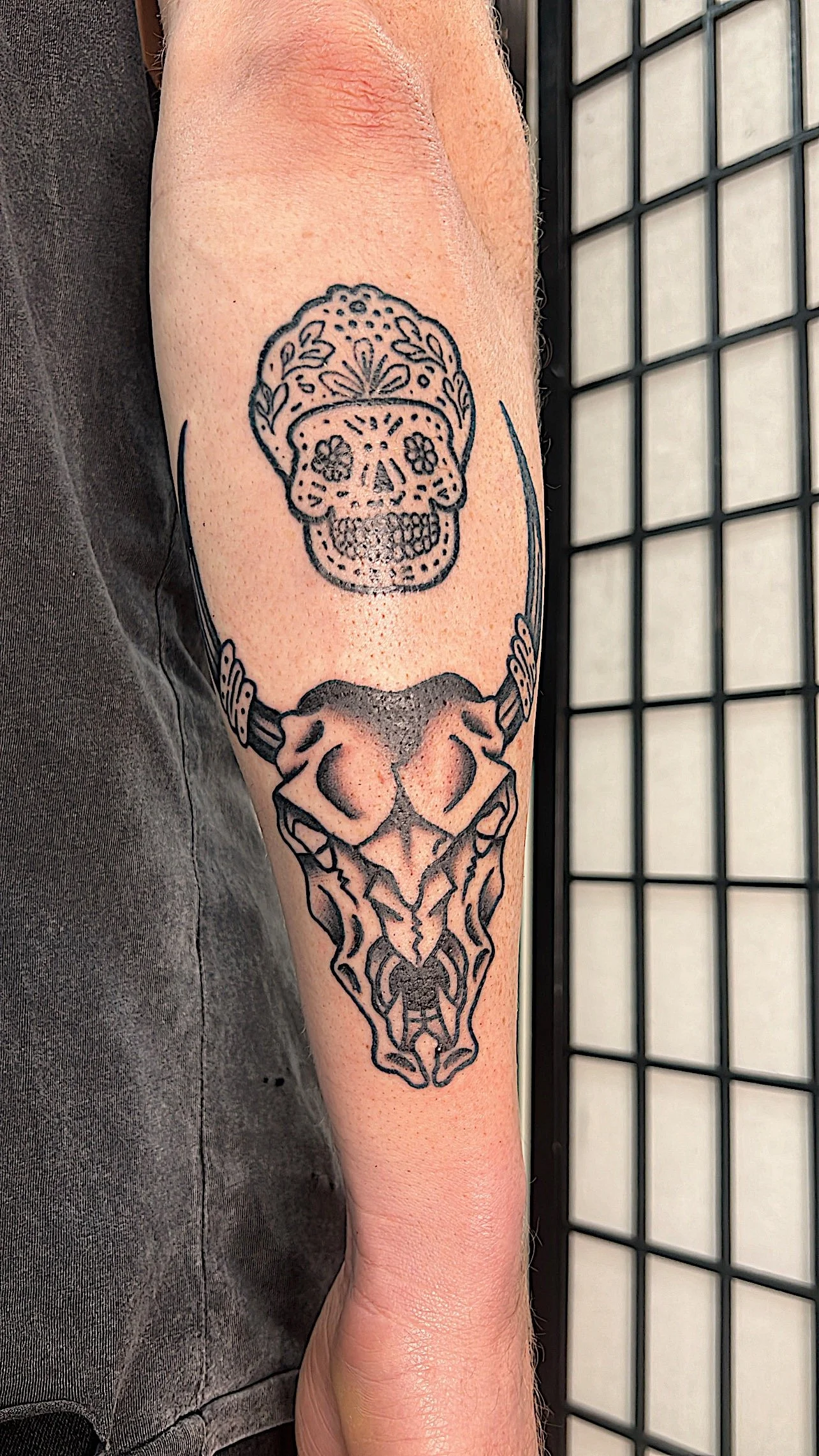 Tattoo of a sugar skull above a stylized demon skull on a person's forearm.