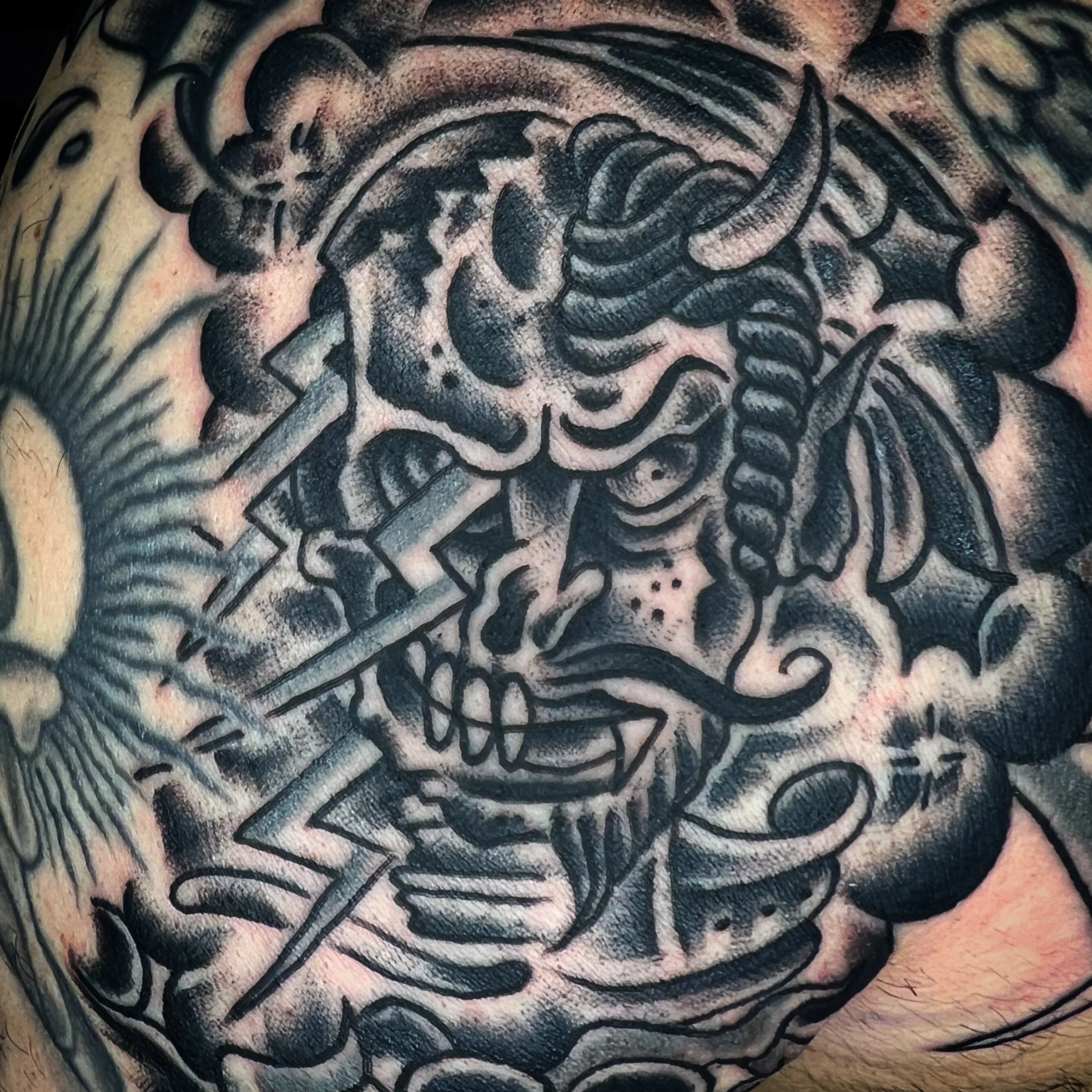 A tattoo of a skull with horns and a lightning bolt, surrounded by dark clouds and abstract elements.