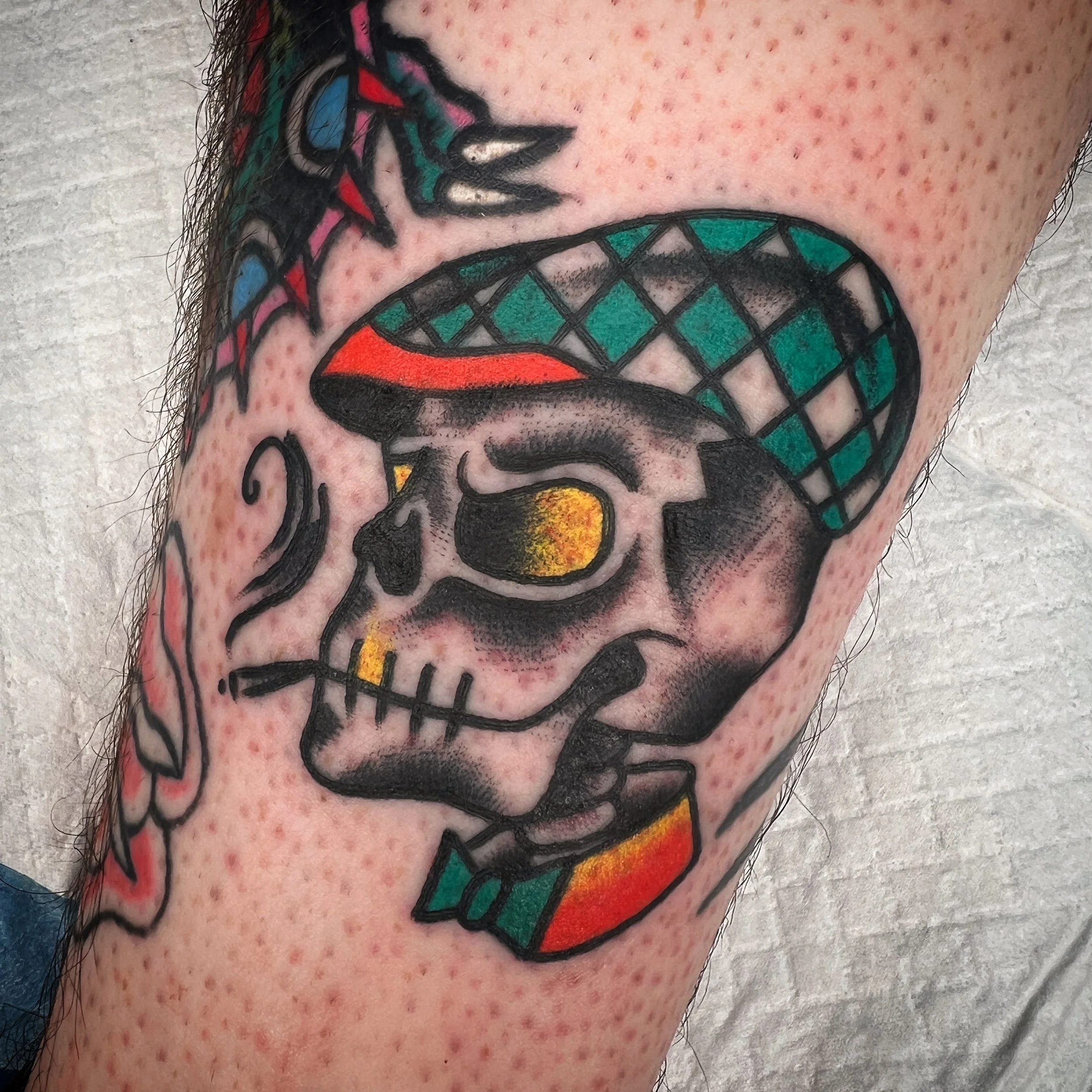 Tattoo of a skeleton with a hat that has a diamond pattern, featuring red, green, and yellow colors.