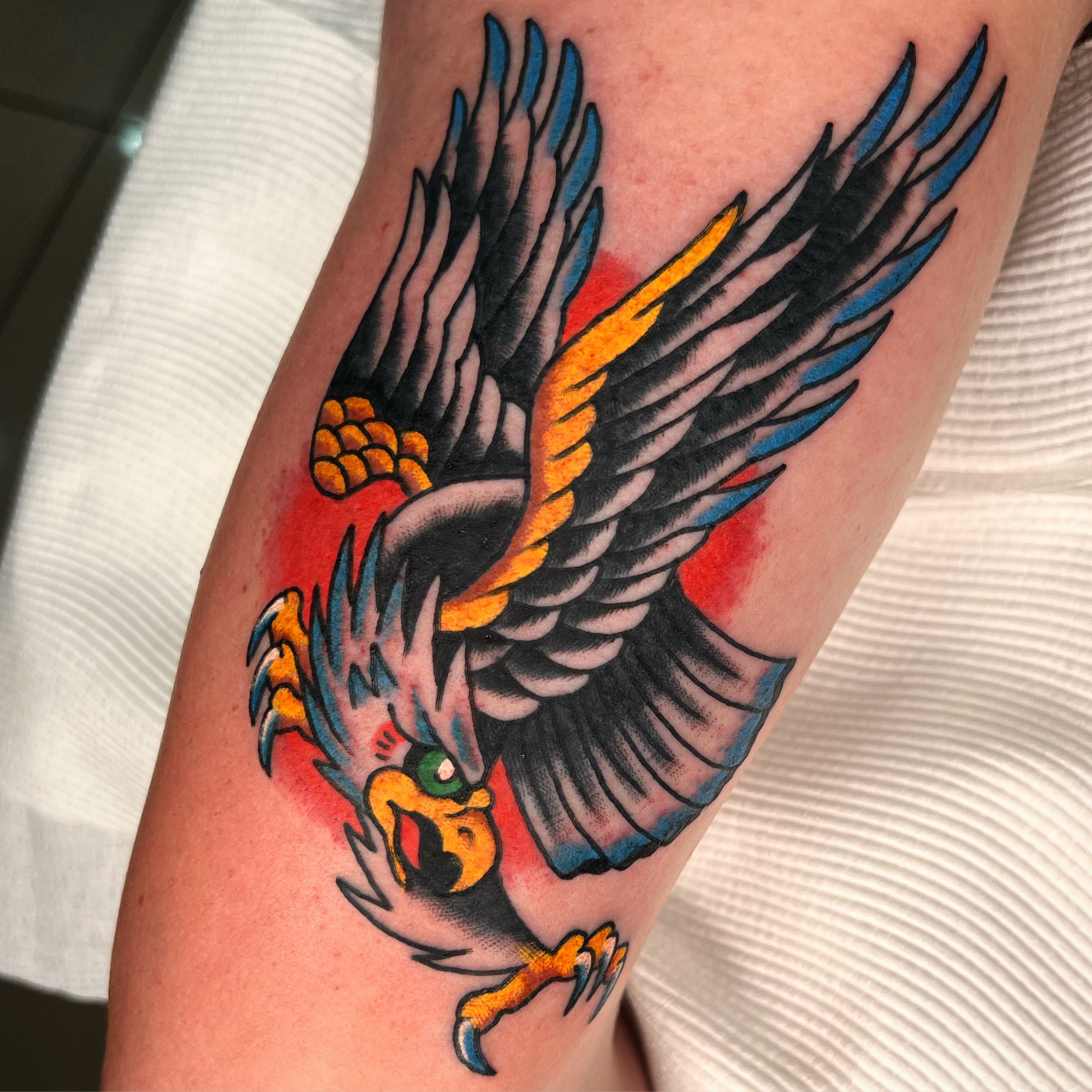 Tattoo of an eagle with black, blue, and yellow wings, and a fierce expression.