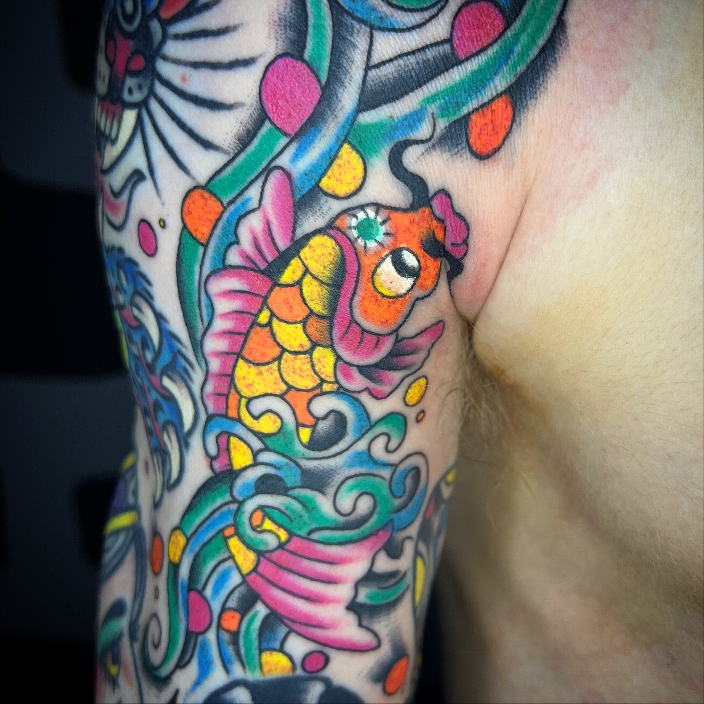 Colorful tattoo of a fish swimming among waves on person's arm.