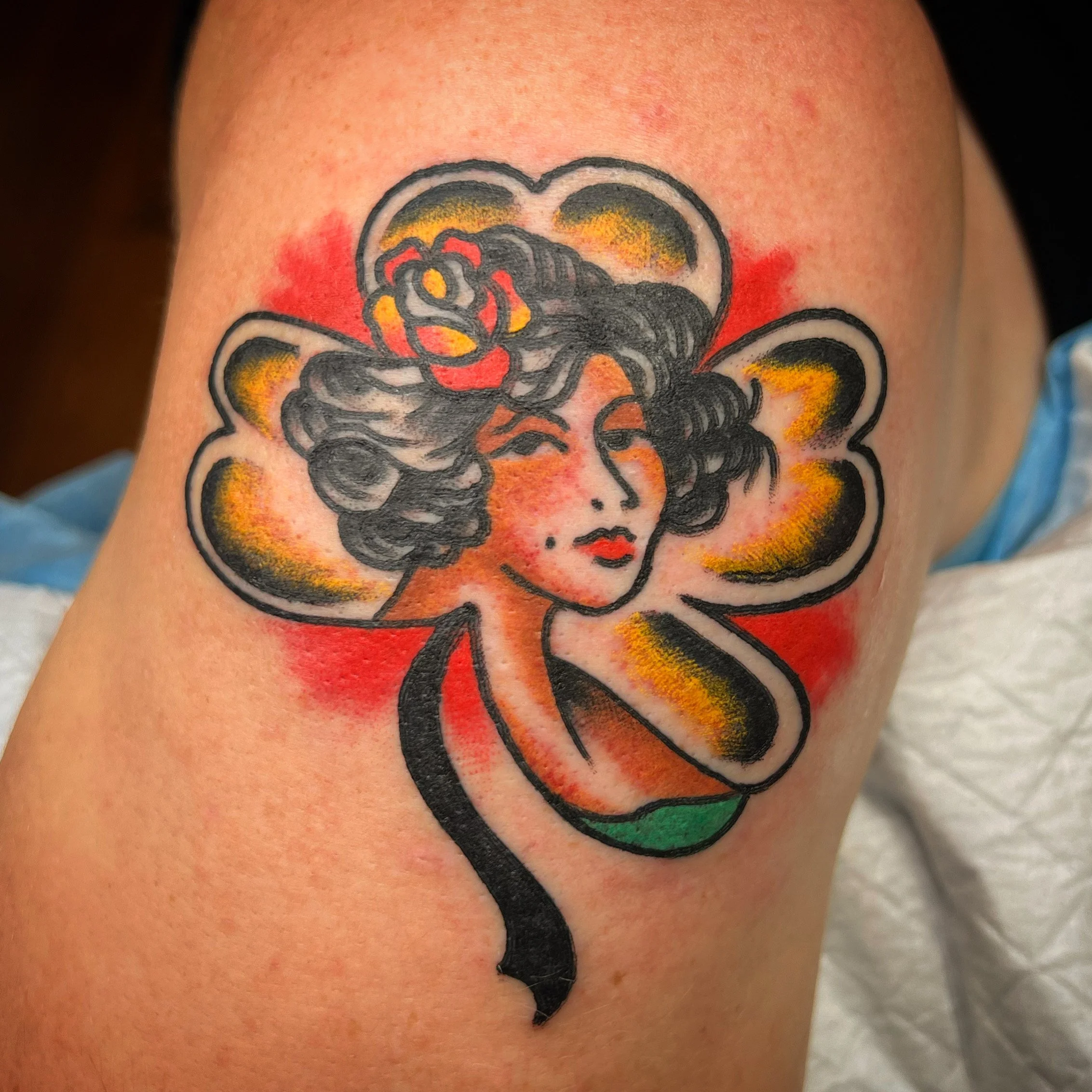 Tattoo of a woman's face with wavy hair, red lips, and a flower in her hair, surrounded by colorful abstract background.