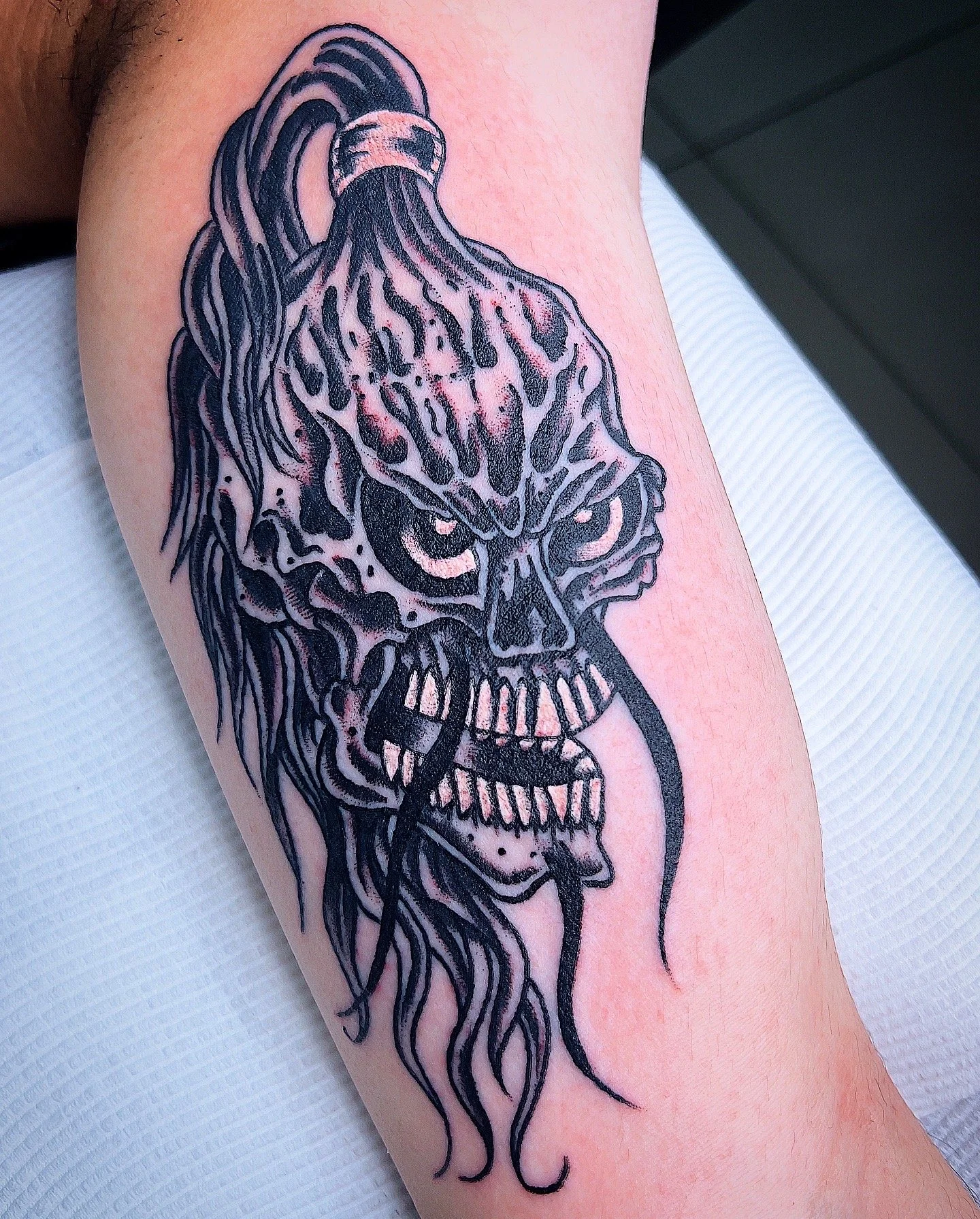 Black line tattoo of a snarling, stylized tiger's head with flowing hair, on a person's arm.