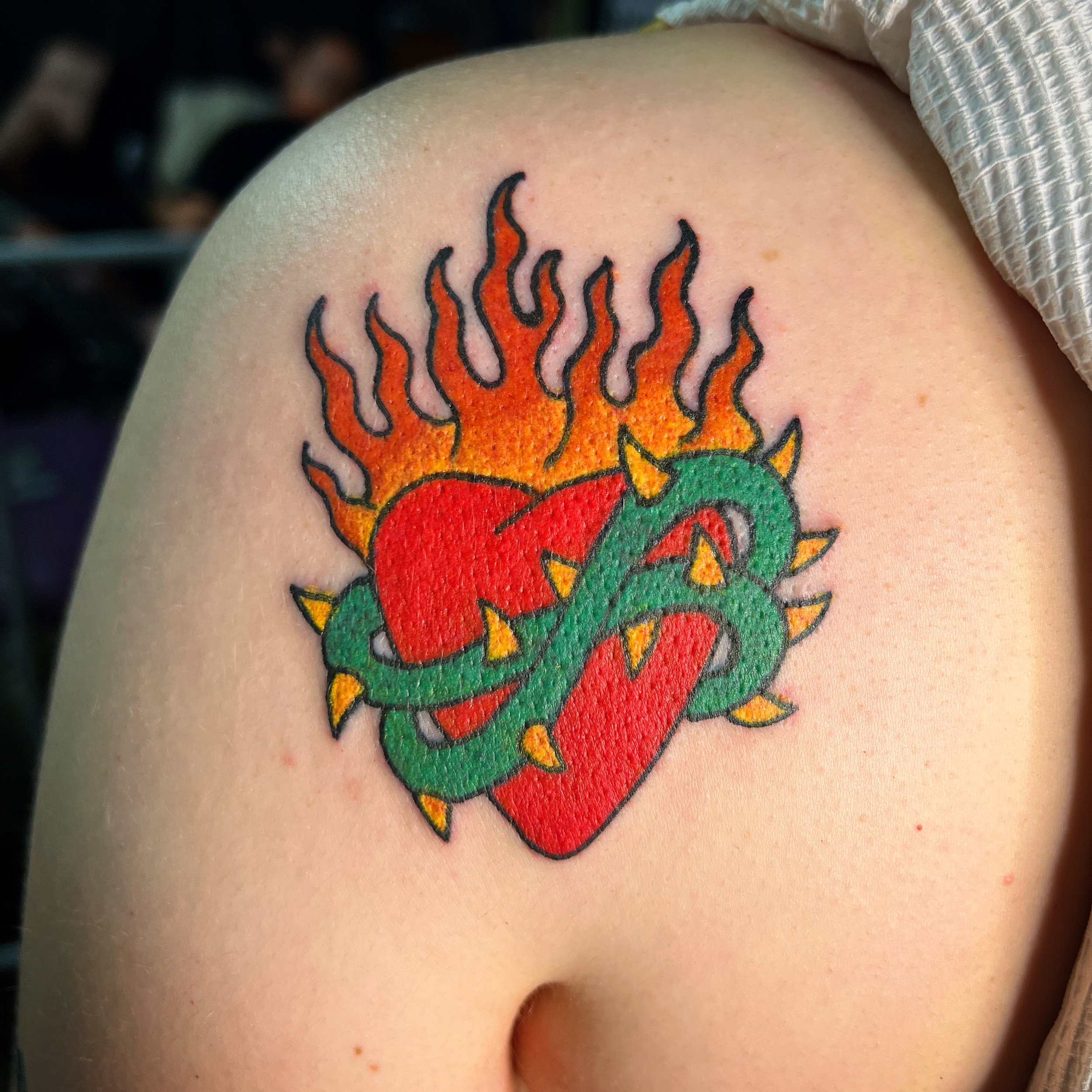 Tattoo of a red heart with a green snake wrapped around it, flames behind the heart, and spikes on the snake.