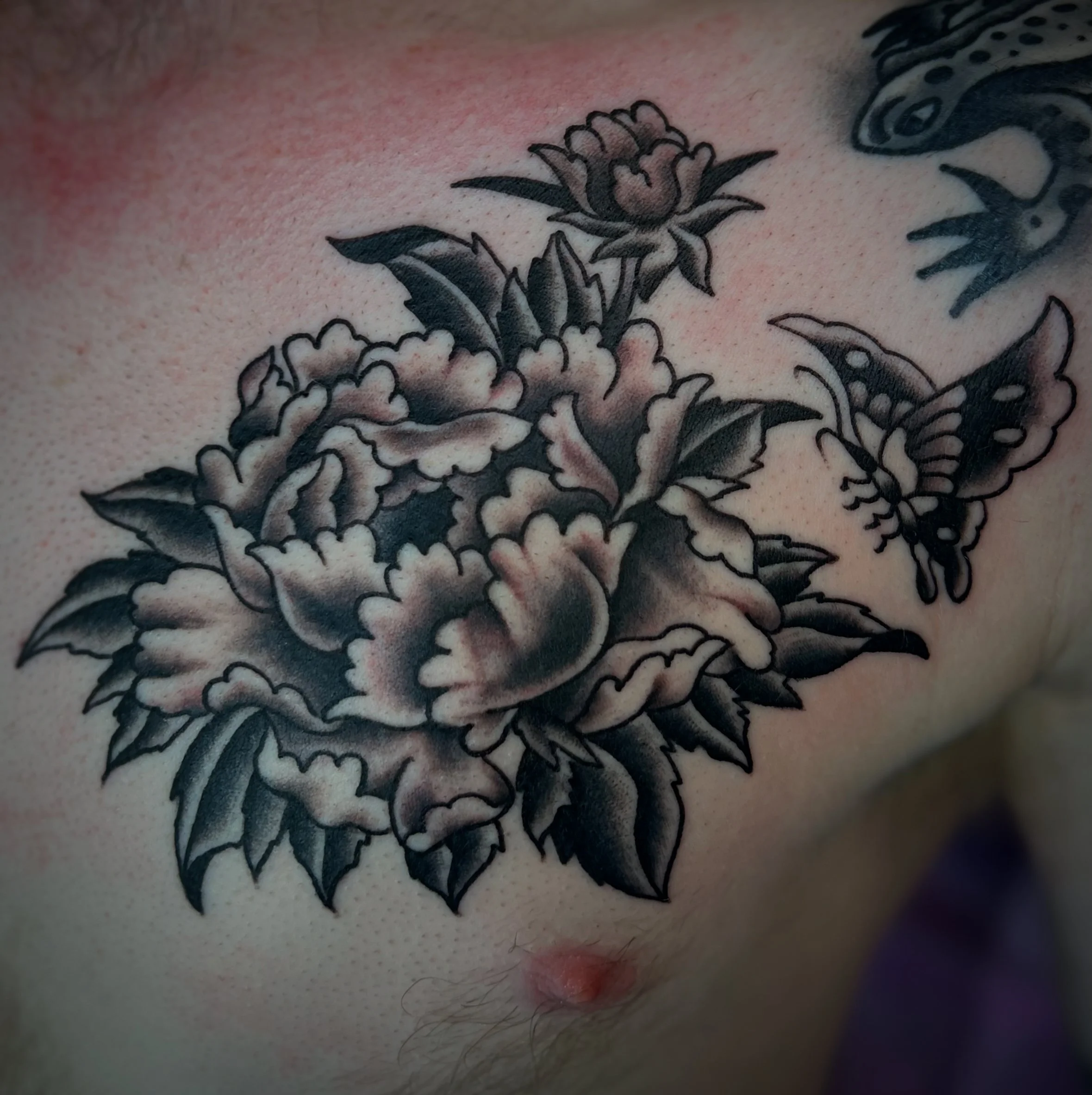 Black and gray tattoo of a blooming flower with leaves and a butterfly on the skin of a person's chest.