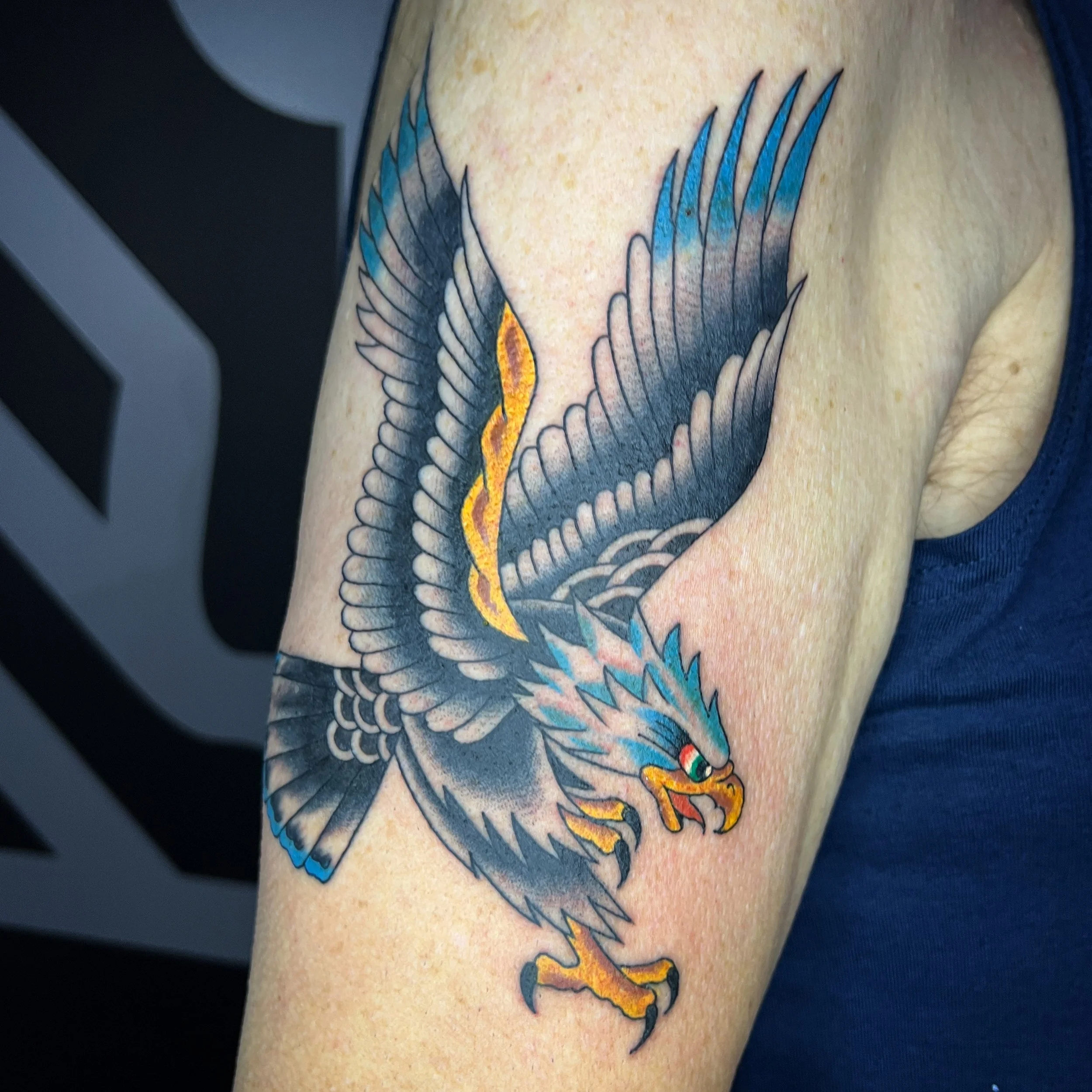 Tattoo of a fierce, colorful eagle with spread wings on person's upper arm.