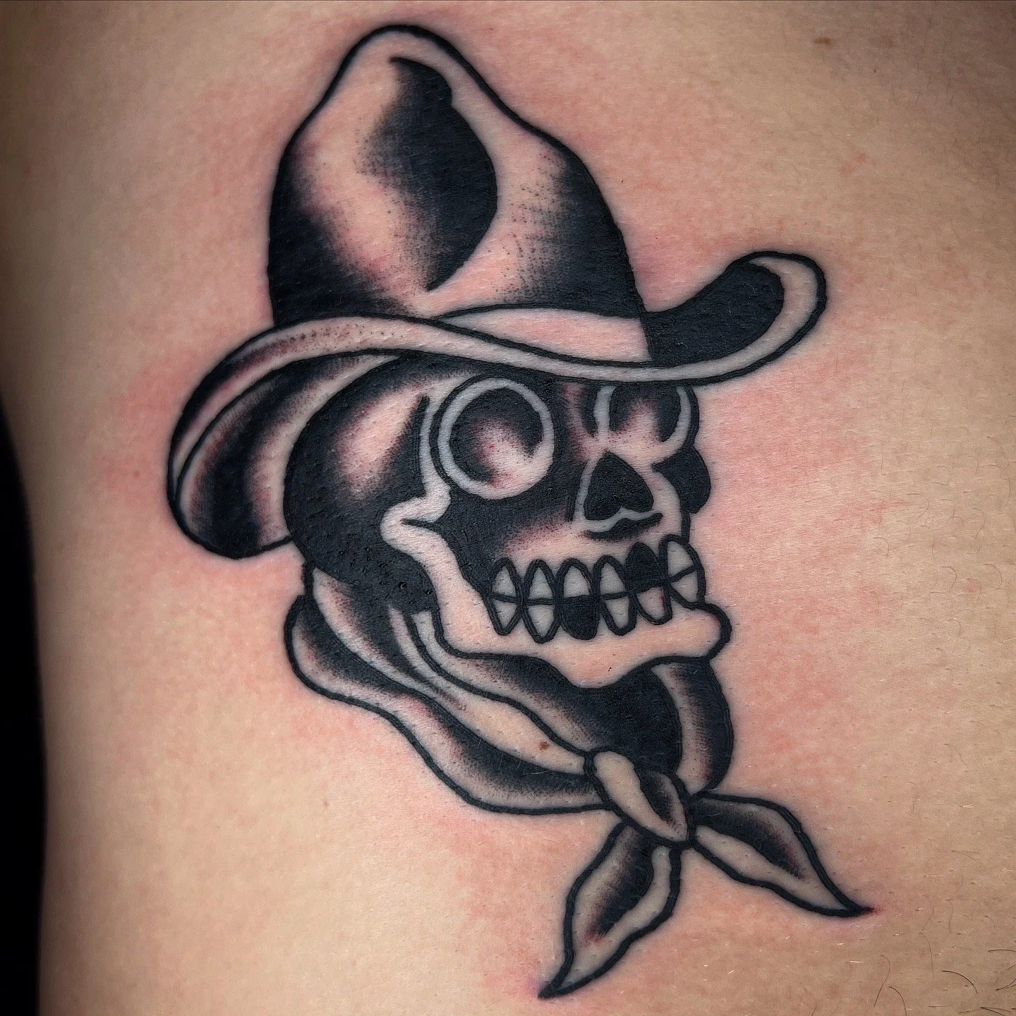 Tattoo of a skull wearing a cowboy hat with a bandana tied around its mouth.