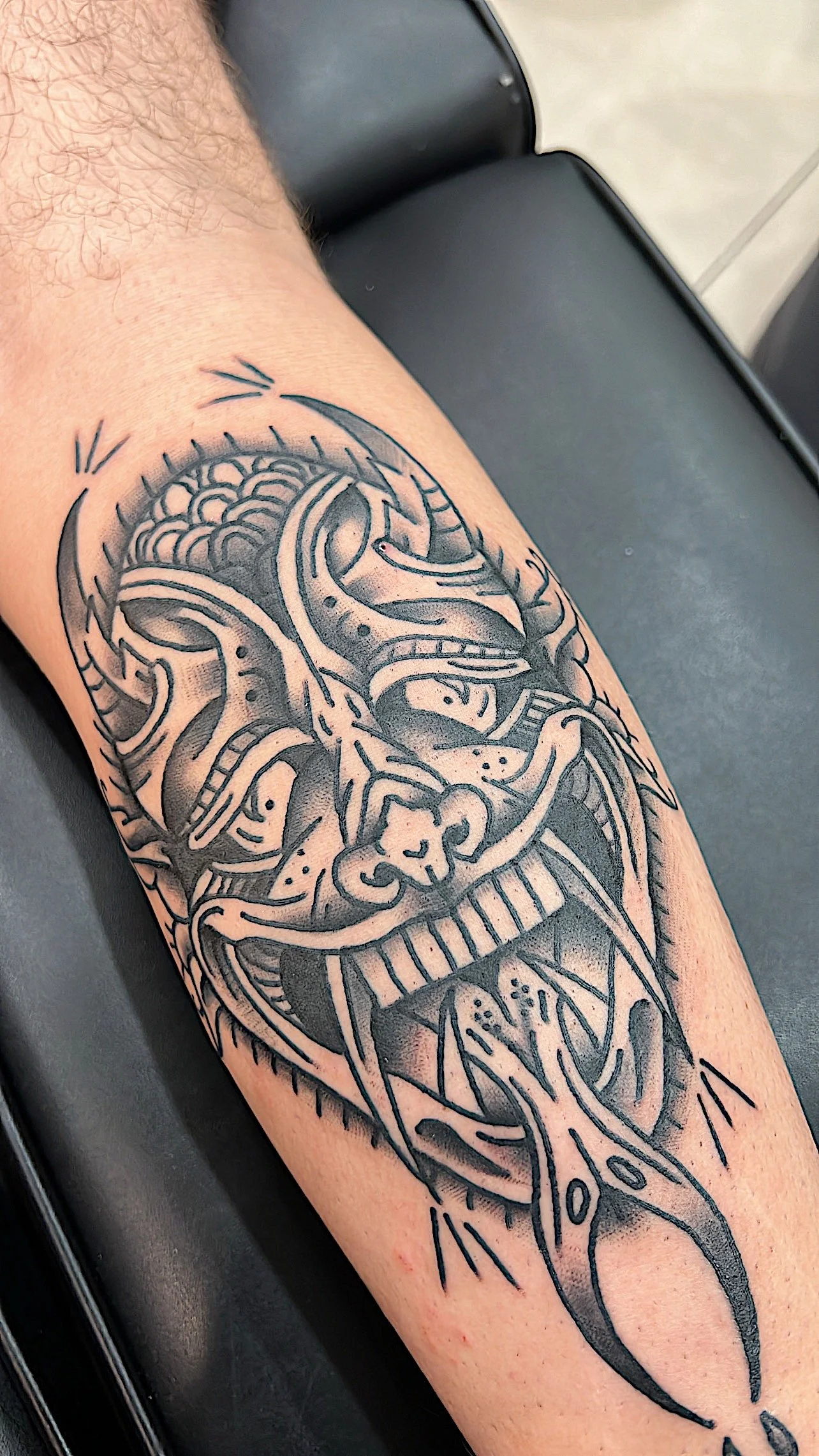 Black and gray tattoo of a fierce dragon with wide eyes and sharp teeth on a person's arm.