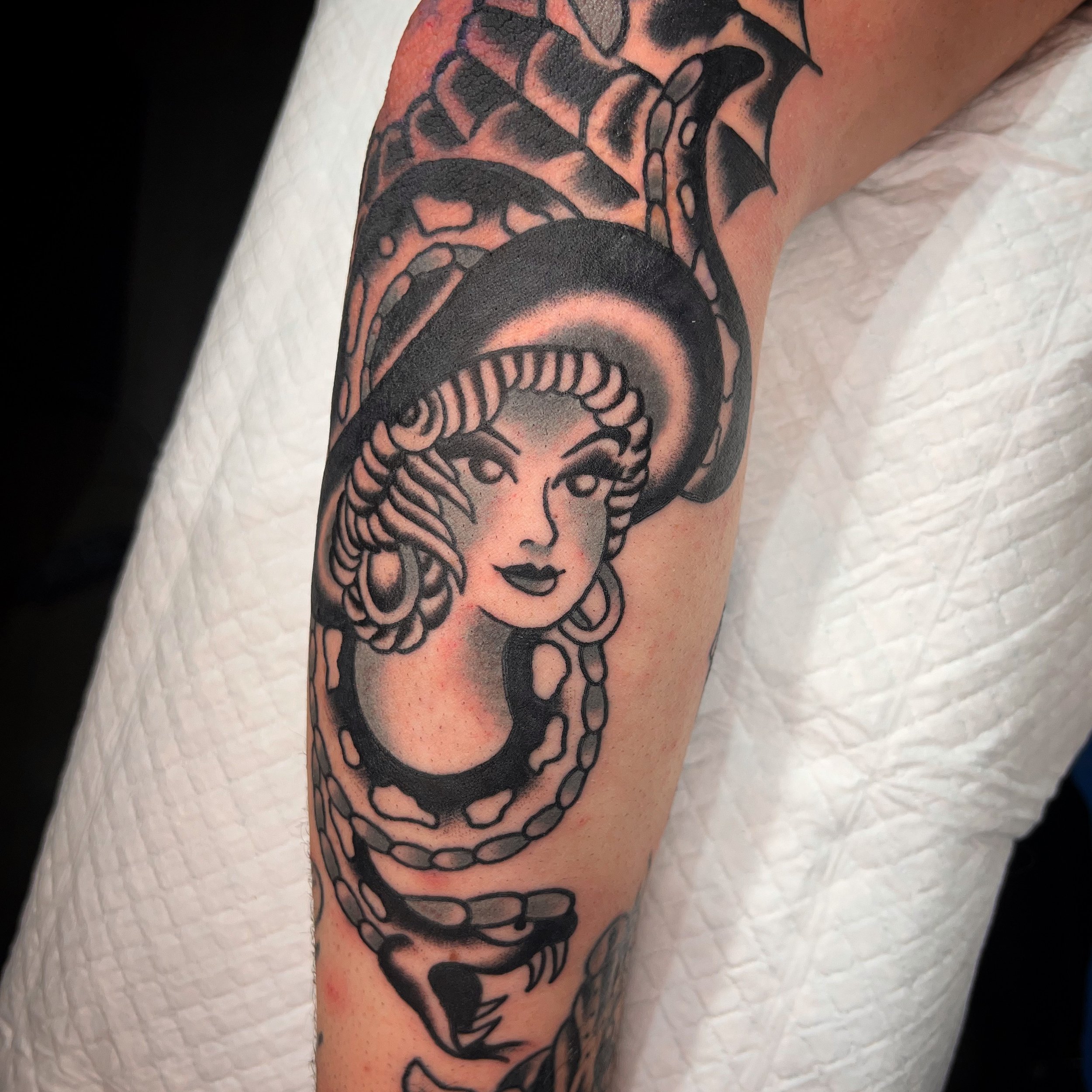 Black and gray tattoo of Medusa with snake hair on person's upper arm.