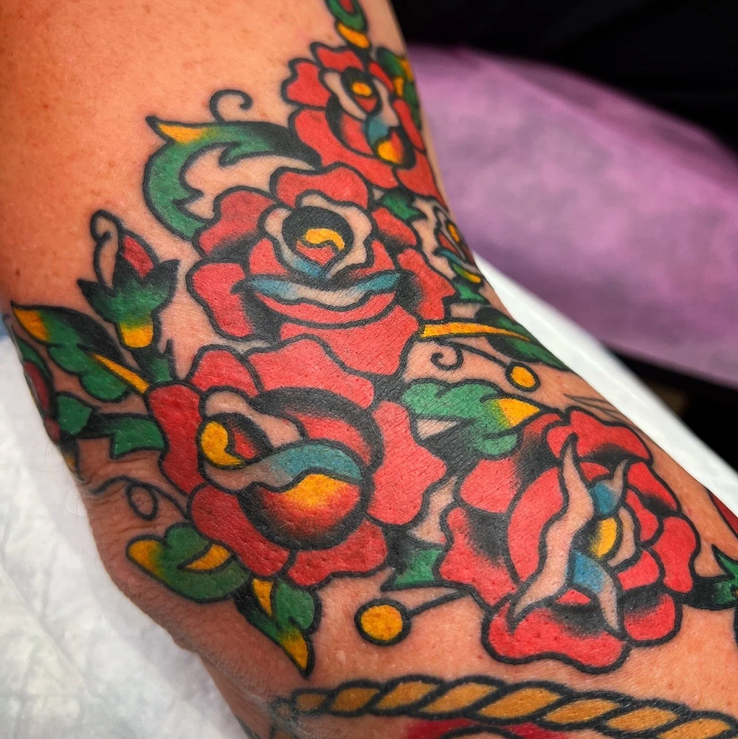 Close-up of a colorful tattoo featuring large red roses with green leaves and yellow accents on skin.