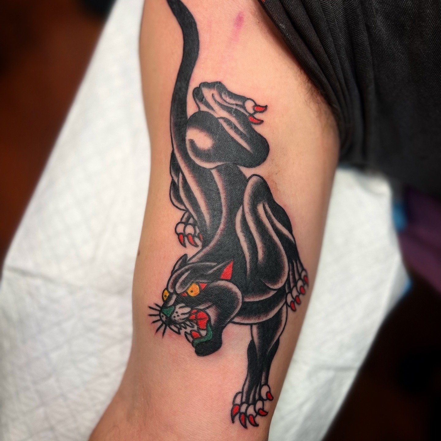 A colorful tattoo of a black panther with yellow eyes, red tongue, and red claws on a person's upper arm.